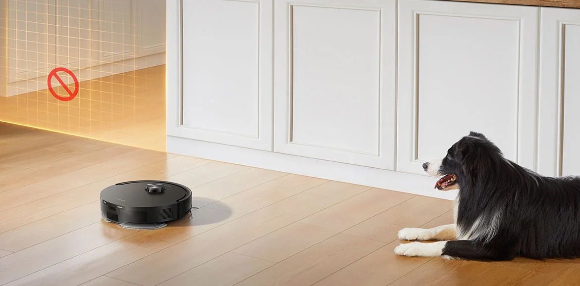 Robot sprzątający na drewnianej podłodze obok leżącego psa. Widoczna jest wirtualna ściana.