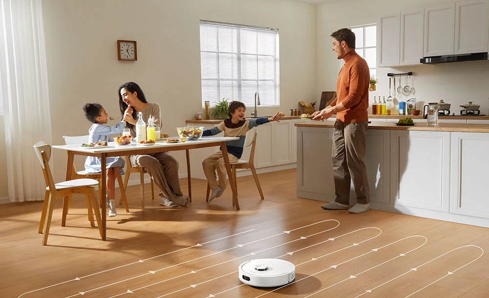 Rodzina je przy stole, podczas gdy robot sprzątający czyści podłogę.