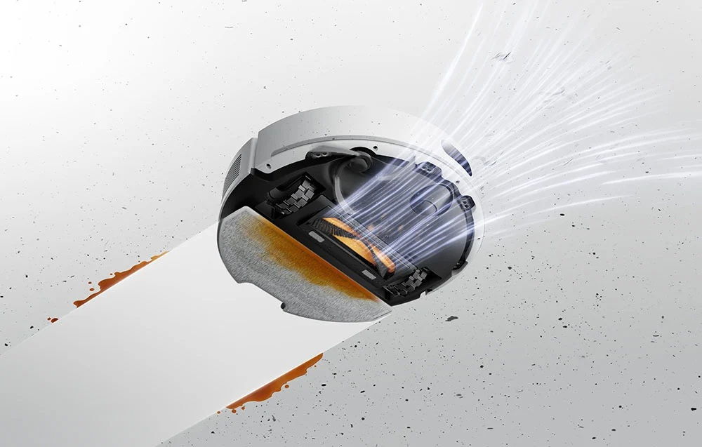 Robot sprzątający zasysa brązowy płyn z białej powierzchni.