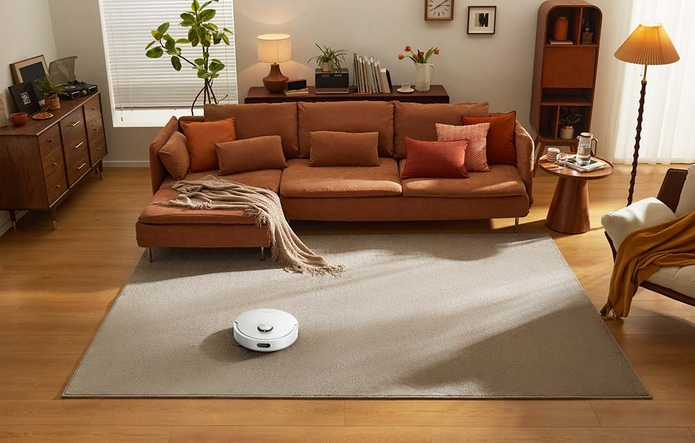Biały robot sprzątający czyści jasnobrązowy dywan w salonie.