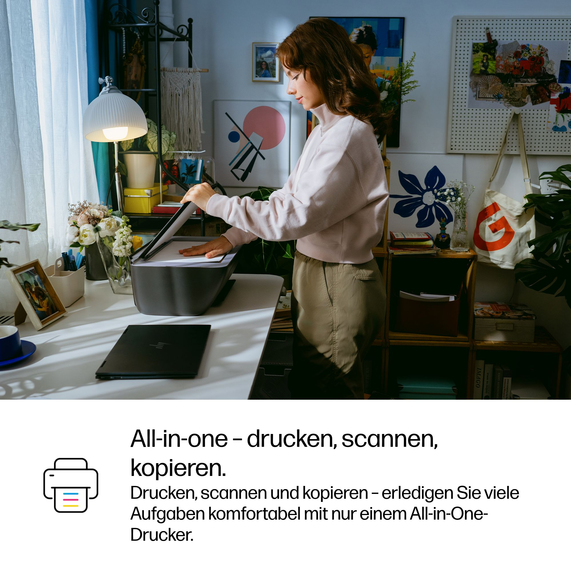 Eine Frau öffnet einen Drucker im Homeoffice, auf dem Schreibtisch liegen ein Laptop und Blumen.