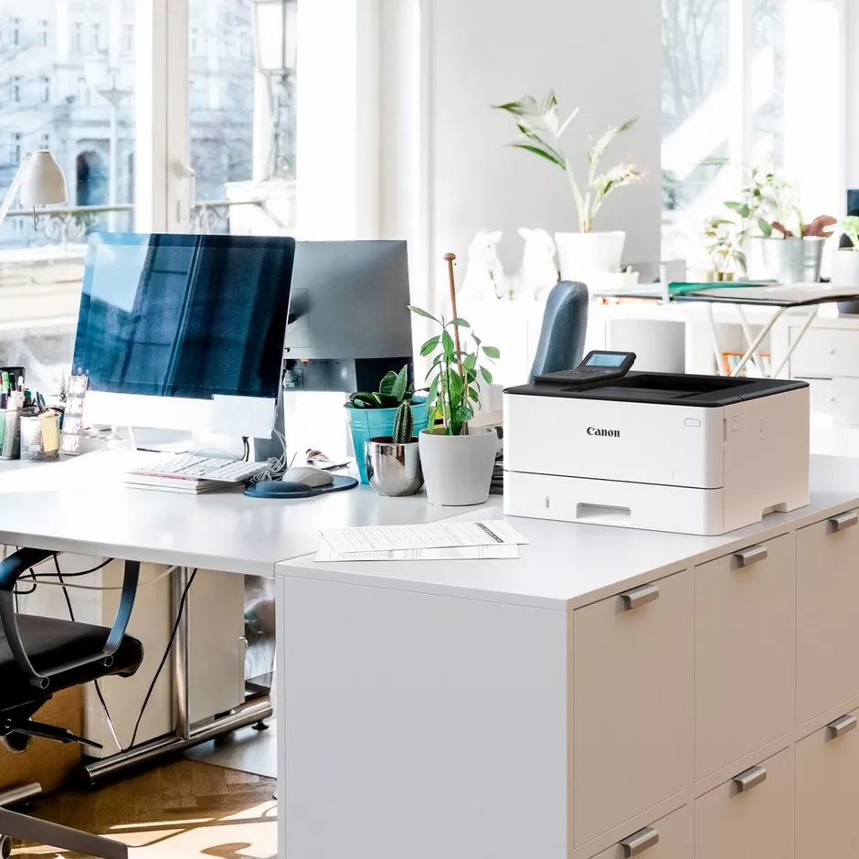 Ein modernes Büro mit Schreibtischen, Computern, einem Drucker und Pflanzen.