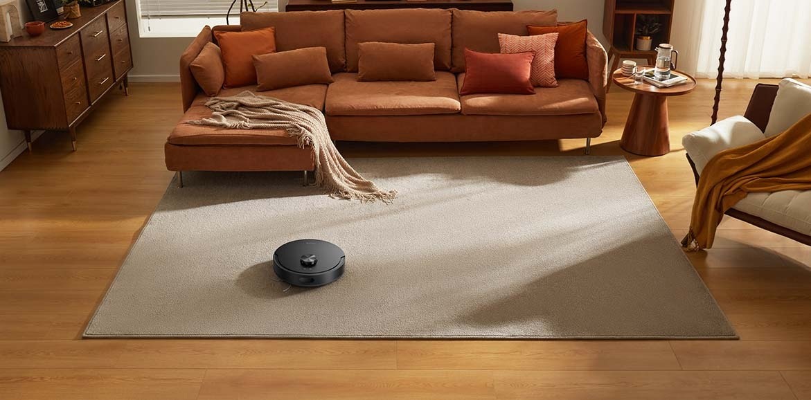 Czarny robot sprzątający czyści jasną dywan w salonie.