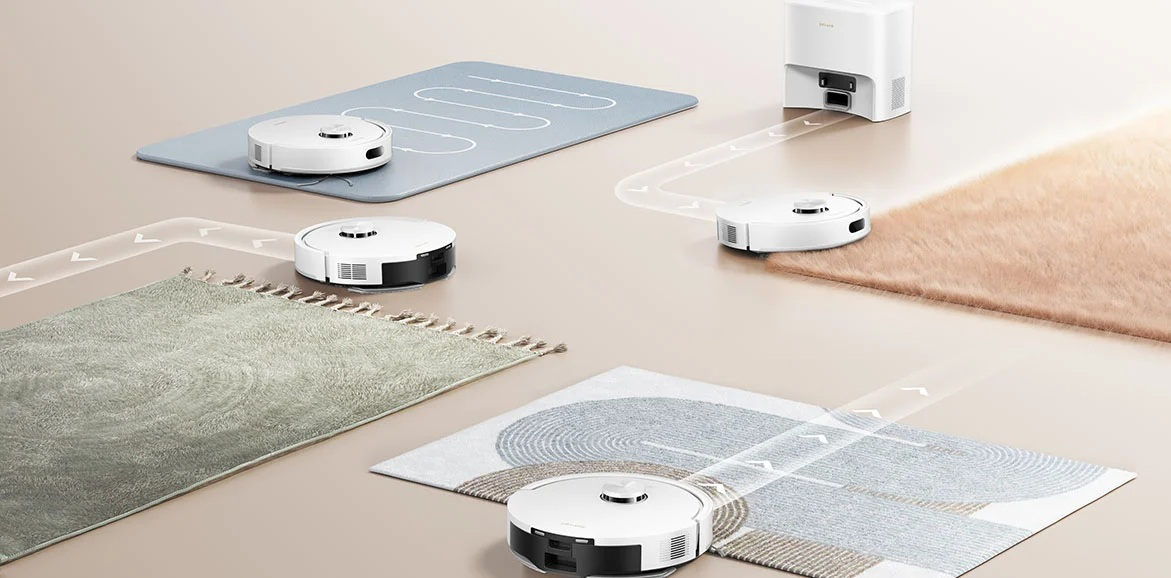 Białe roboty sprzątające czyszczą dywany, jeden dokuje do stacji.