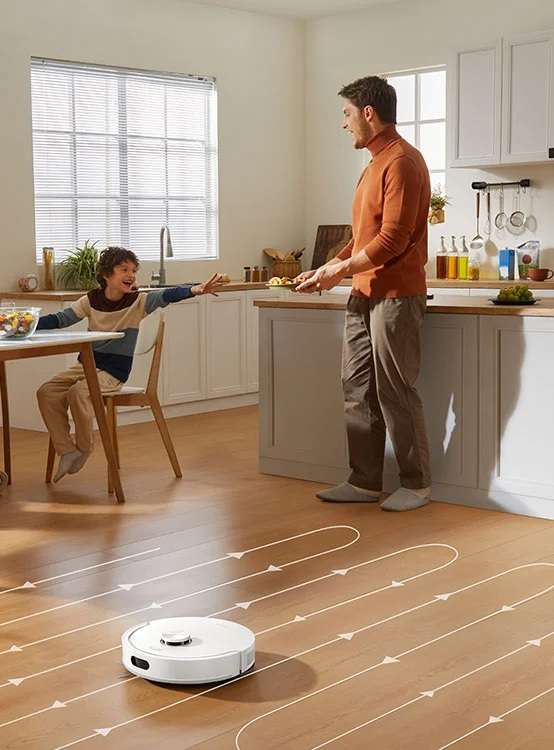 Odkurzacz automatyczny czyści drewnianą podłogę w kuchni, podczas gdy ojciec rozmawia z synem.
