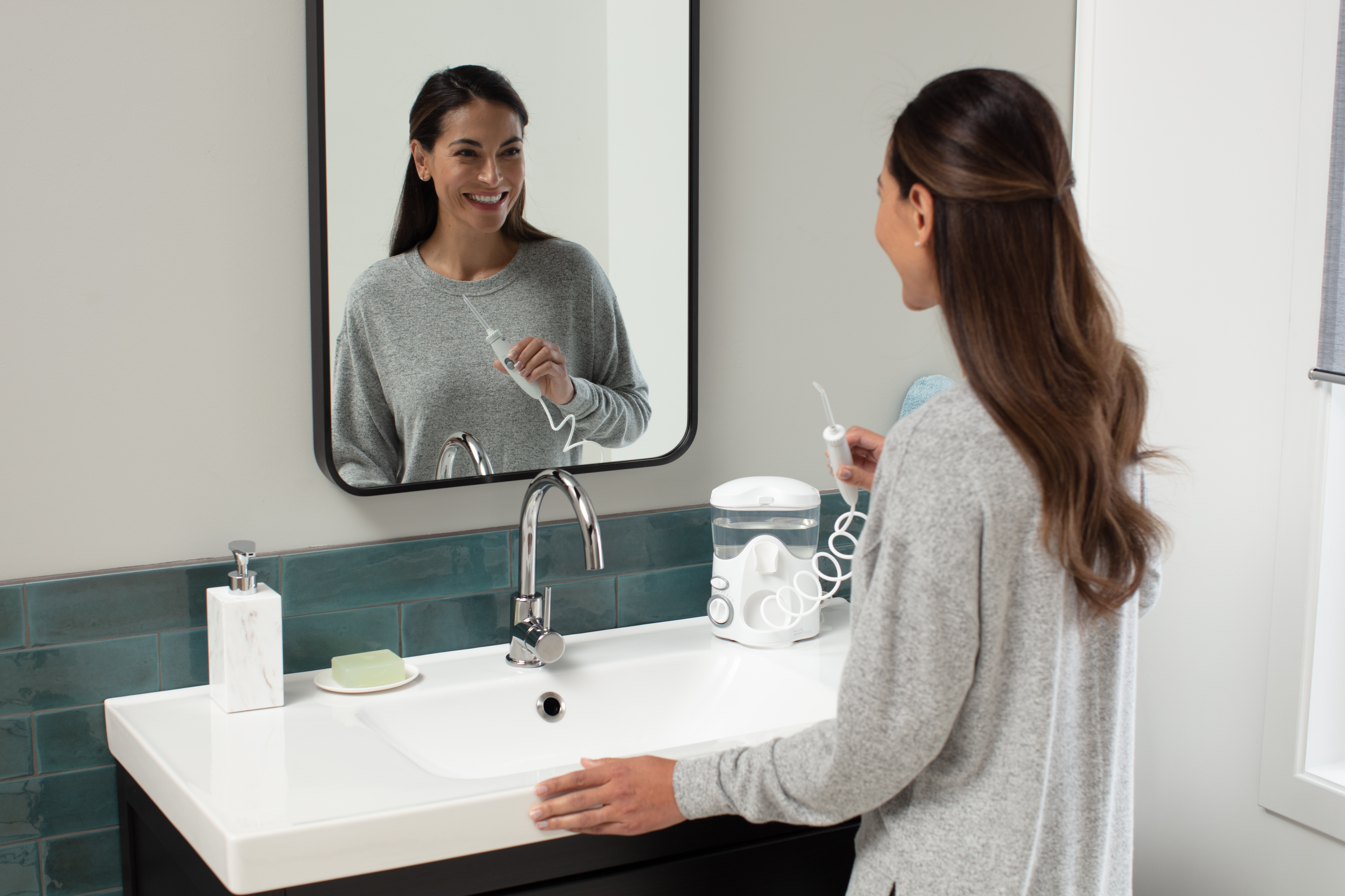 Kobieta z irygatorem wodnym w łazience przed lustrem.