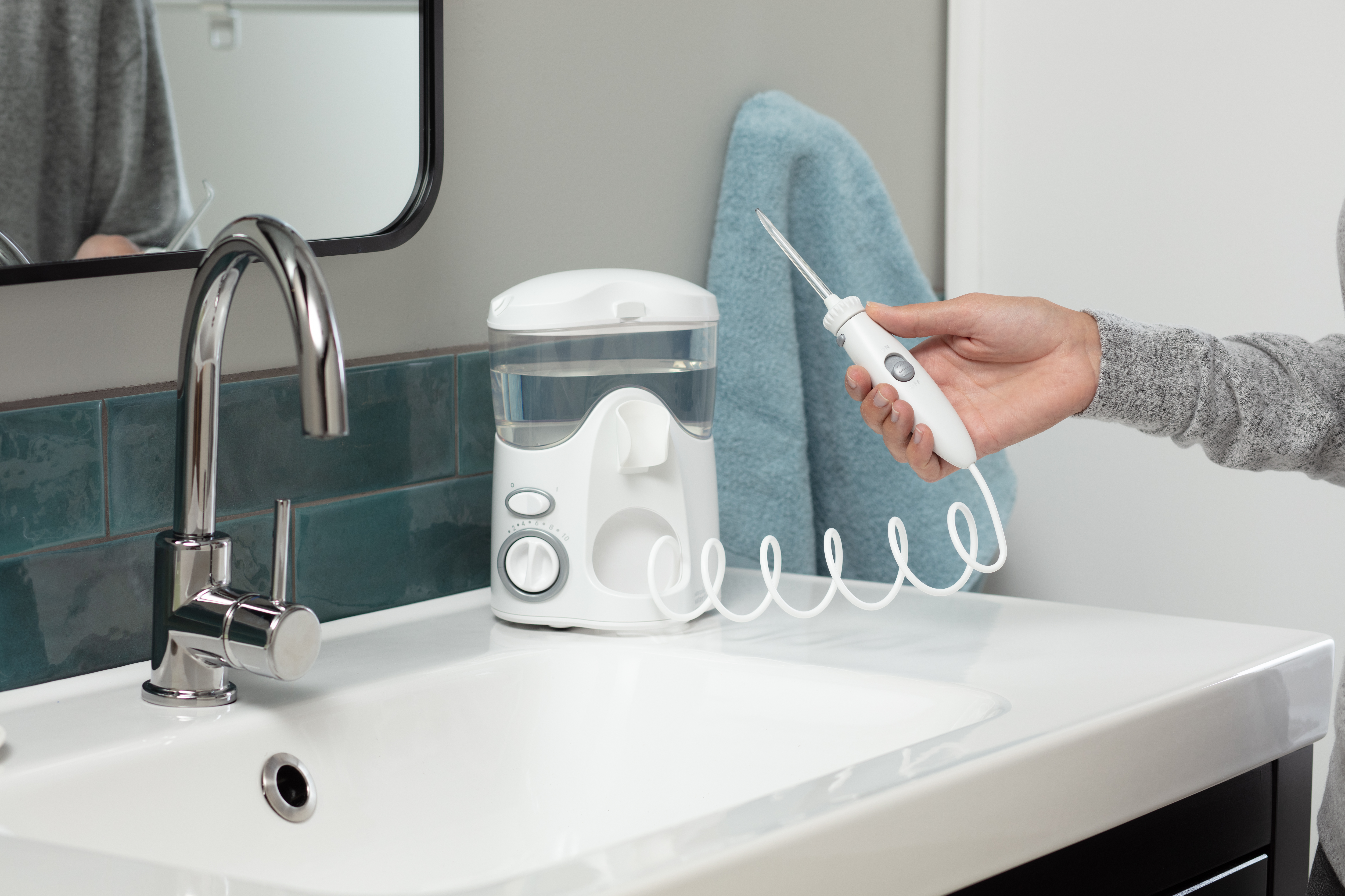 Biała irygator do zębów z pełnym zbiornikiem stoi na umywalce.