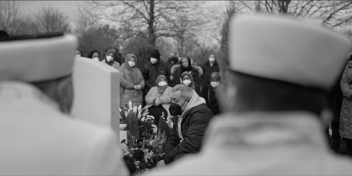 Menschen in Winterkleidung und Masken stehen bei einer Beerdigung.