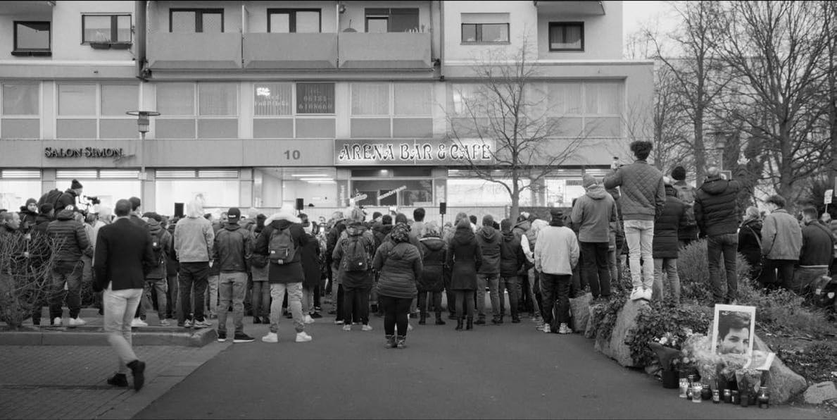 Eine Gruppe von Menschen versammelt sich vor dem „Arena Bar & Cafe“.