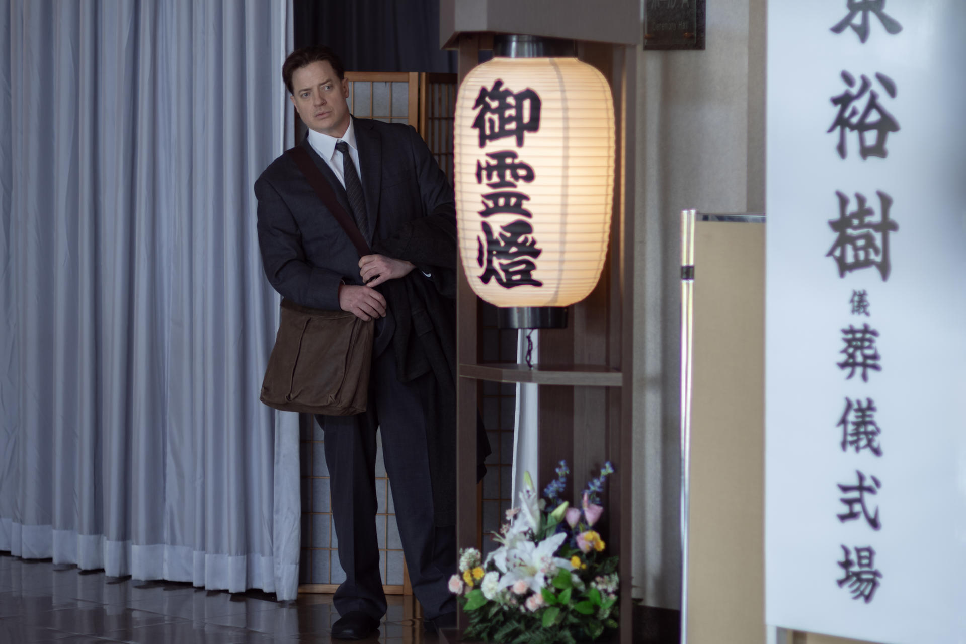 Ein Mann im Anzug steht neben einer Laterne mit japanischen Schriftzeichen und Blumen.