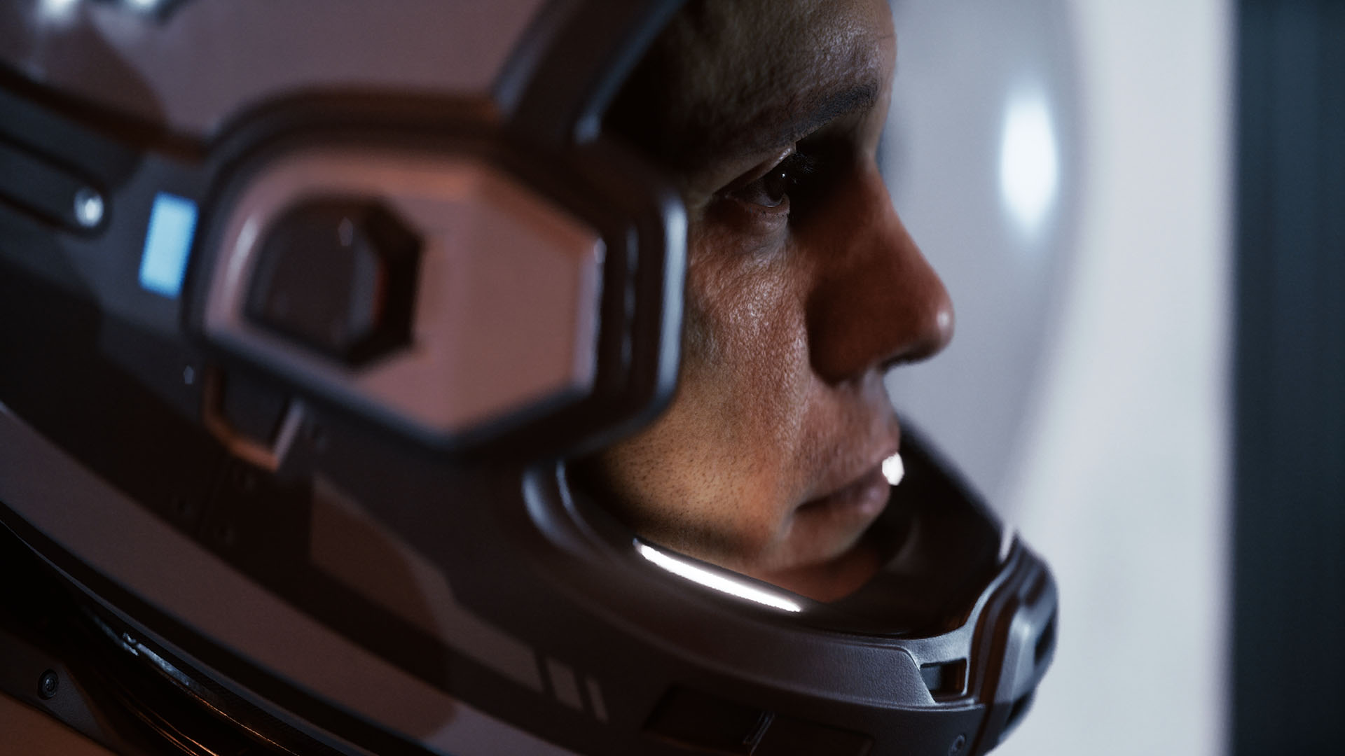 Zbliżenie mężczyzny w skafandrze kosmicznym patrzącego w prawo. Jego kask jest ciemnoszary.