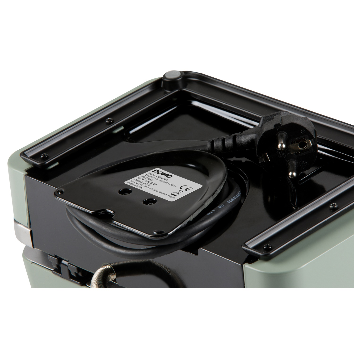 A black power cord with a plug is routed on the underside of a green appliance.