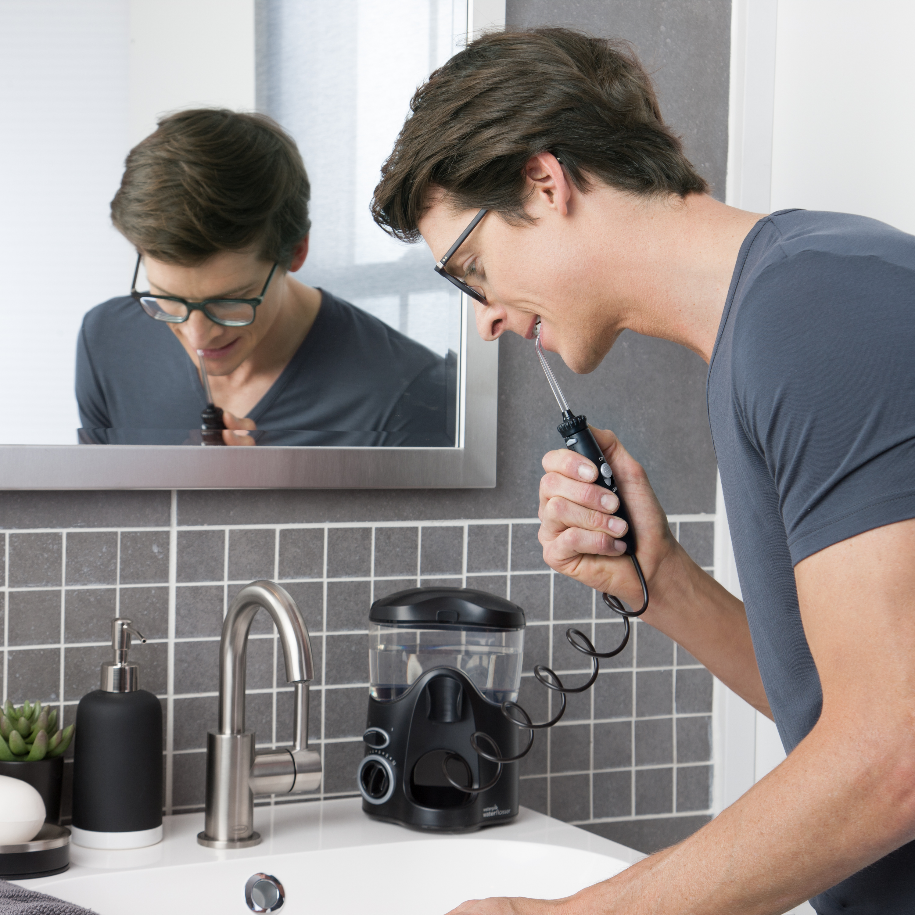 Mężczyzna używa irygatora przed umywalką z lustrem.