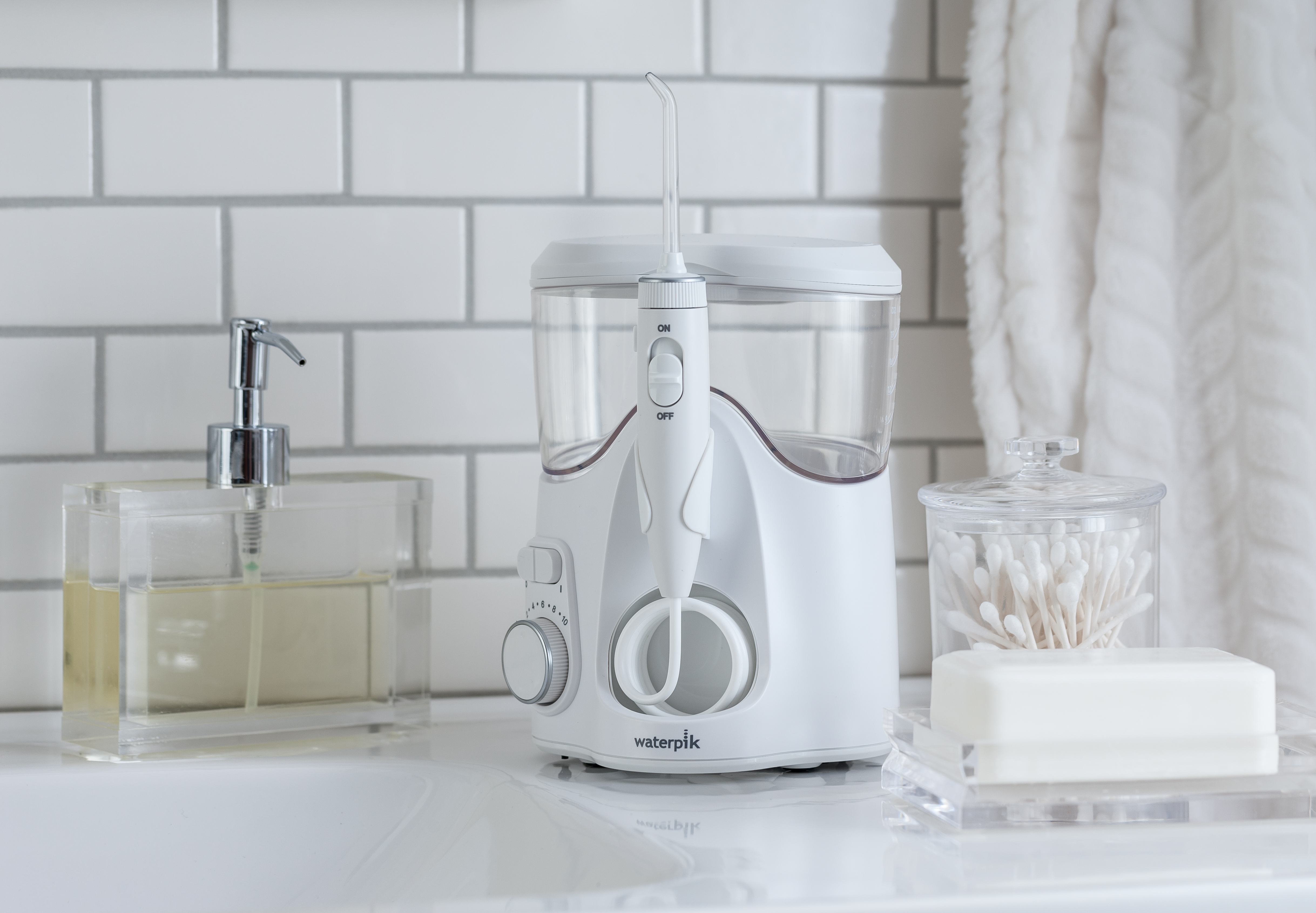 Biała irygator do zębów stoi na blacie z mydłem i wacikami w pobliżu.