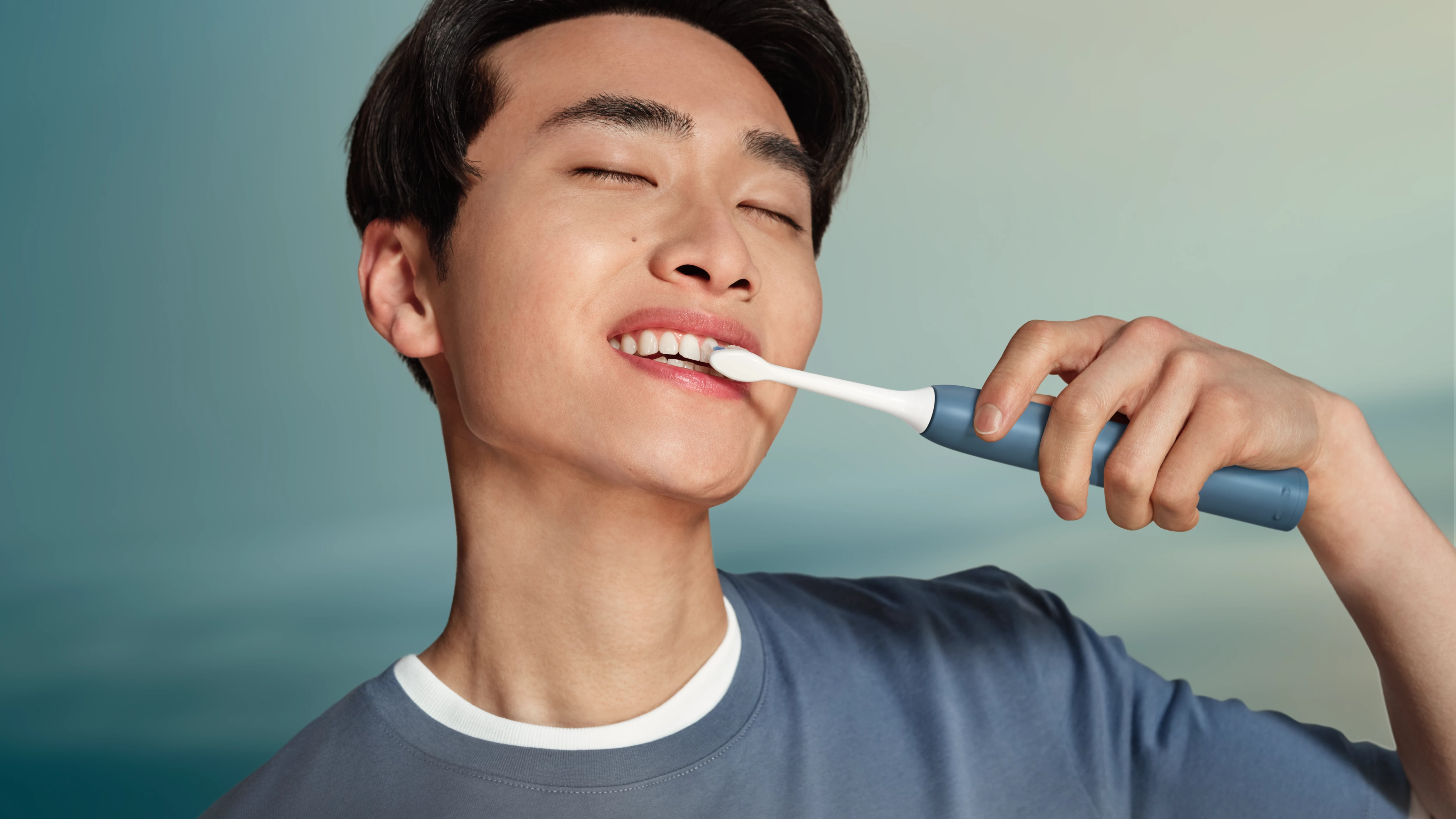 Mężczyzna myje zęby szczoteczką elektryczną na tle niebieskiego nieba.