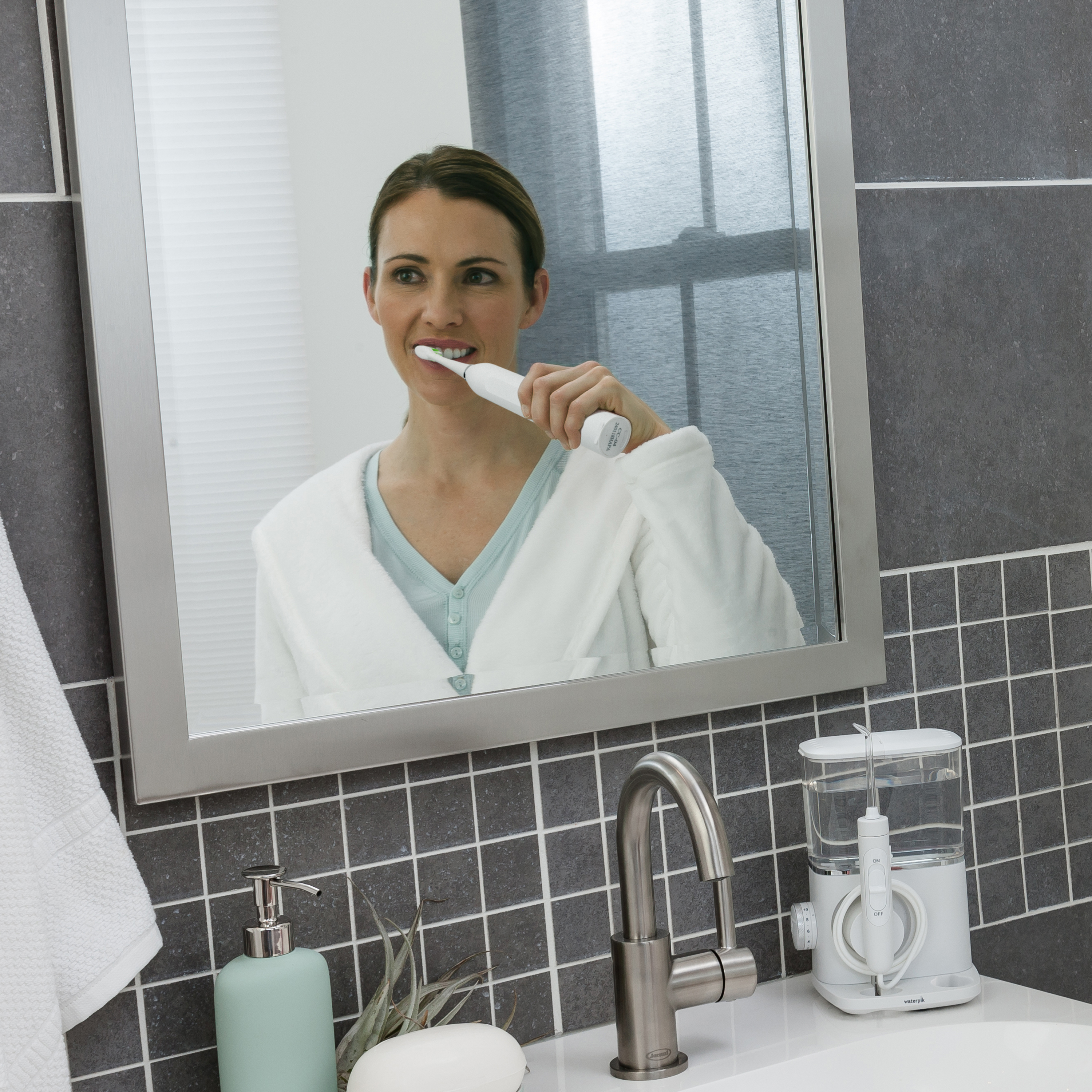 Kobieta myje zęby szczoteczką elektryczną przed lustrem.