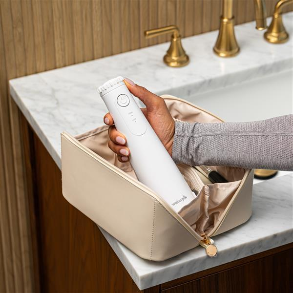 Dłoń trzyma białą irygator nad otwartą kosmetyczką na marmurowym blacie.