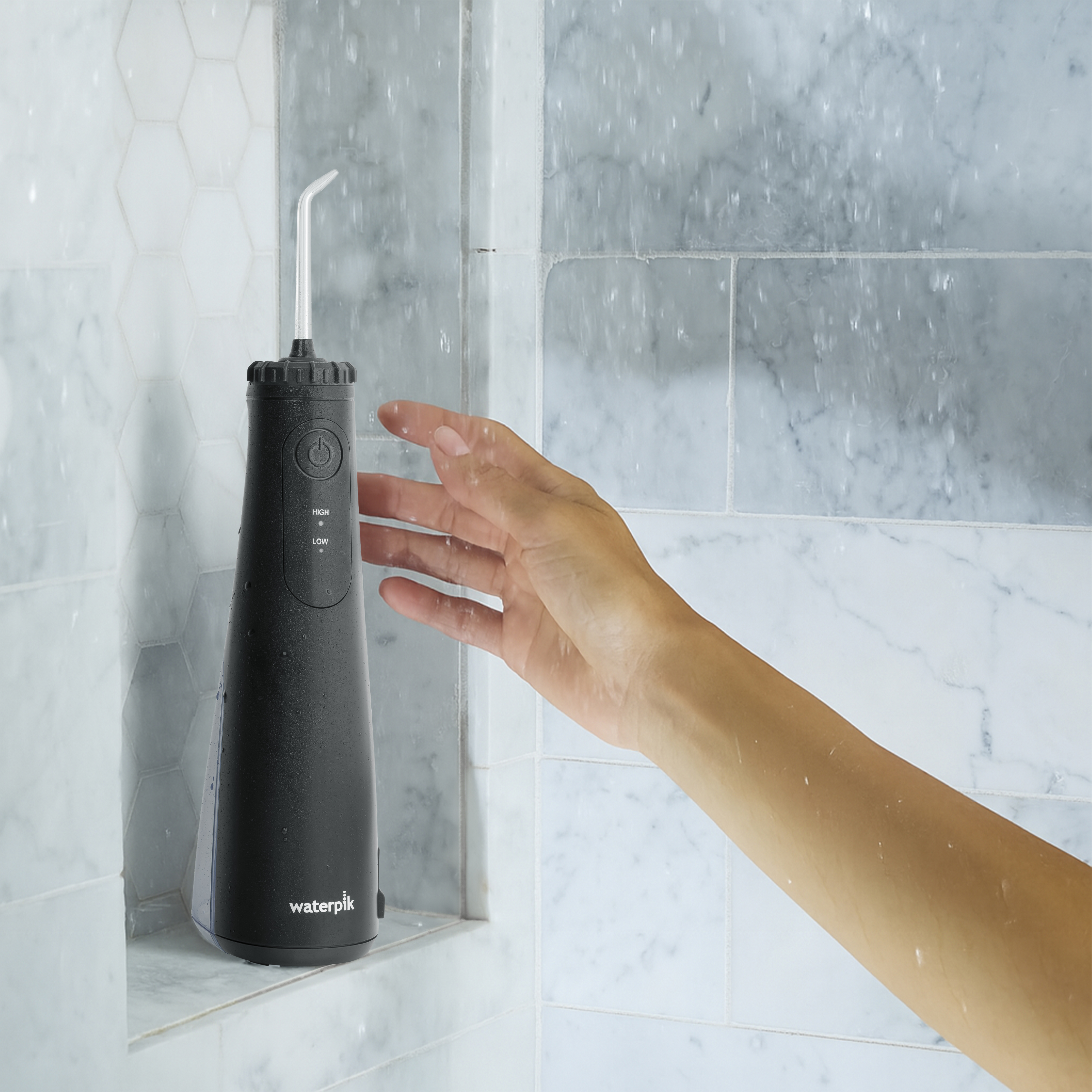 Czarna irygator wodny Waterpik stoi na półce, ręka sięga po niego.
