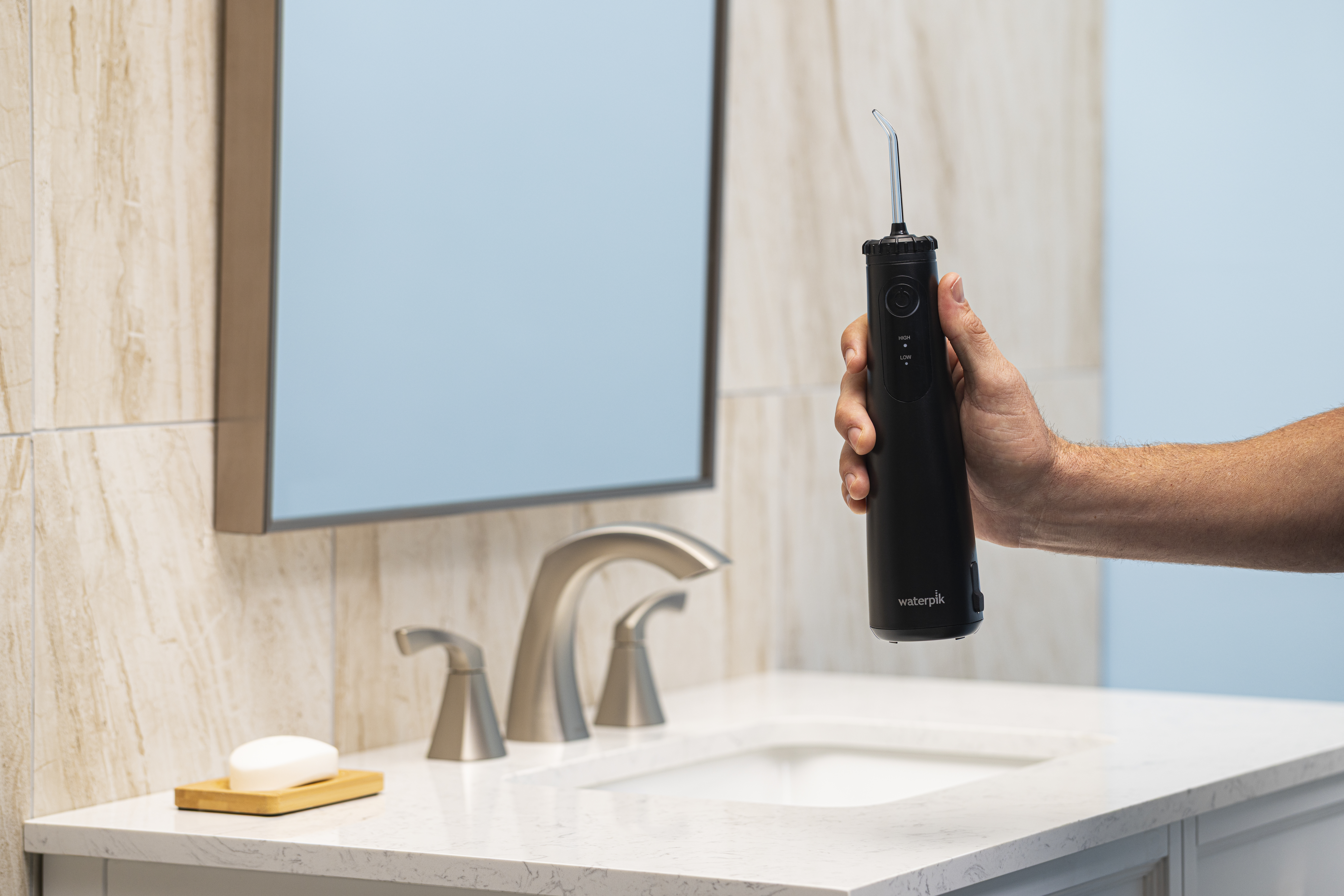 Ręka trzyma czarną irygator dentystyczny nad umywalką łazienkową.