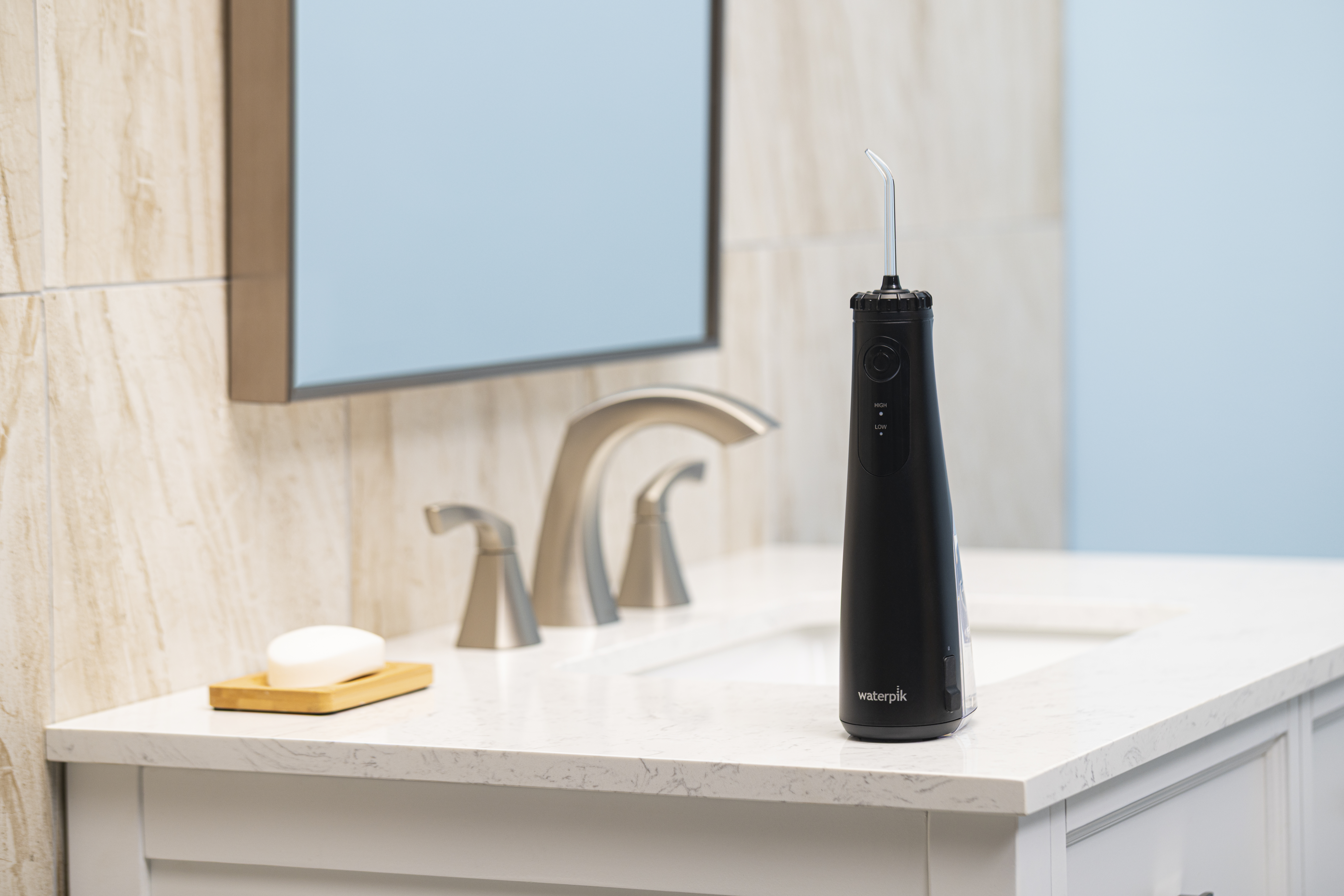 Czarny Waterpik stoi na białym blacie toaletki obok mydła i kranu.