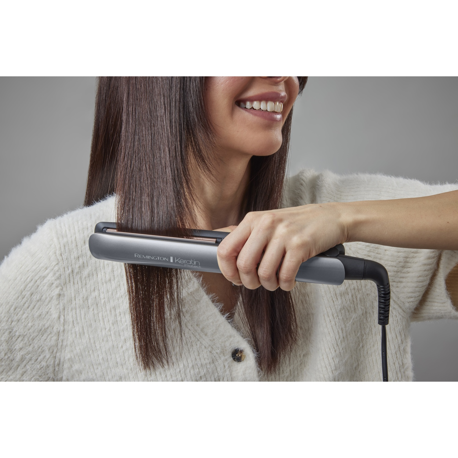 Una donna si liscia i capelli castani con una piastra grigia Remington.