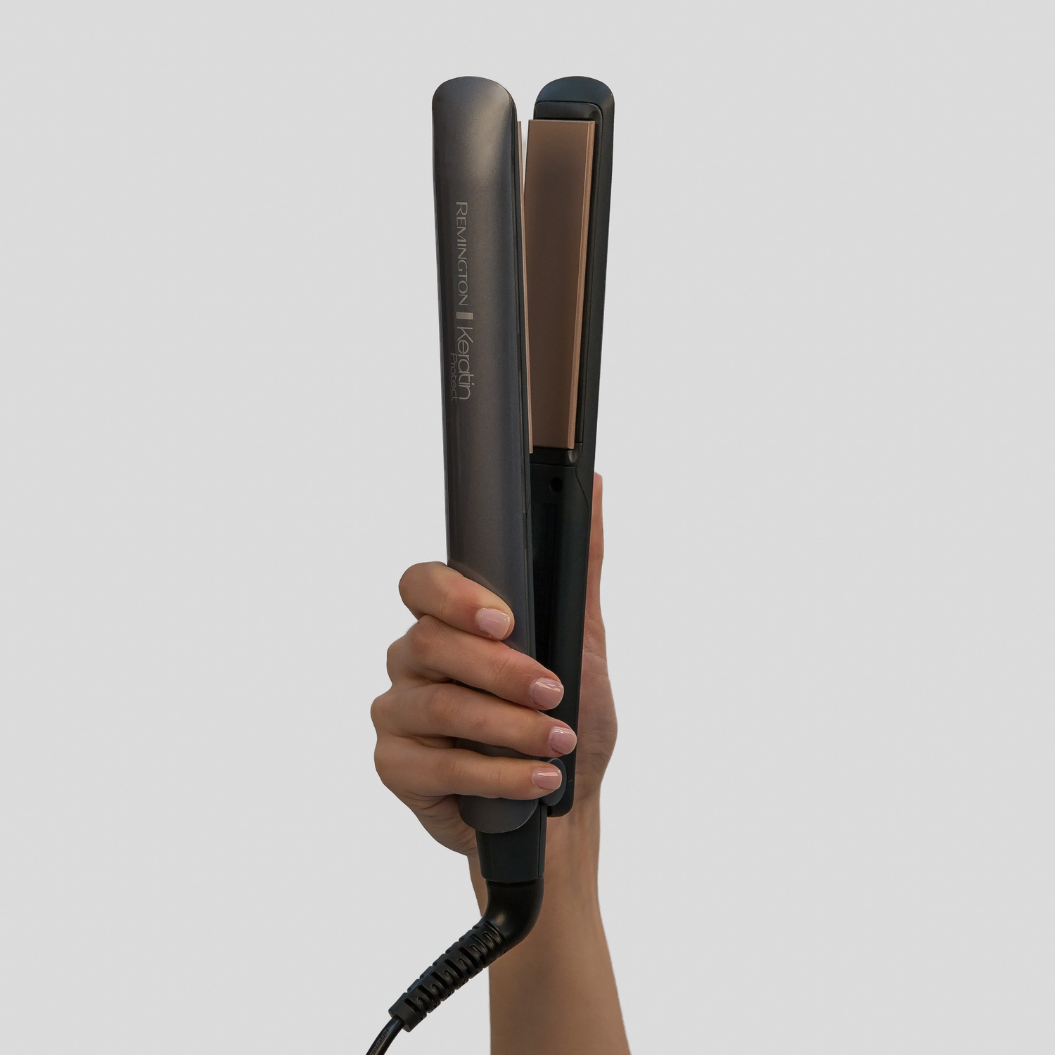 Una mano tiene una piastra per capelli Remington scura con tecnologia Keratina.