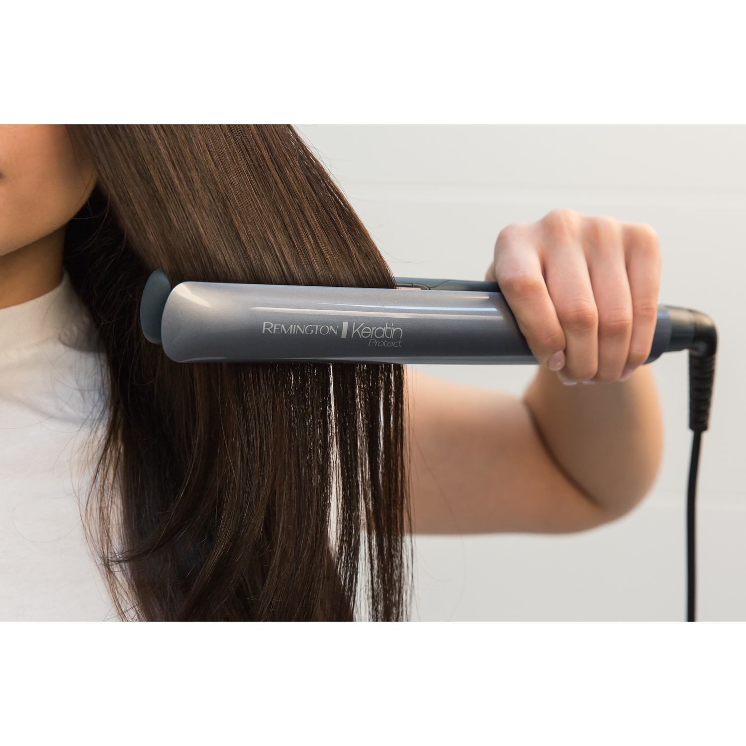 Una persona si liscia i lunghi capelli castani con una piastra Remington.