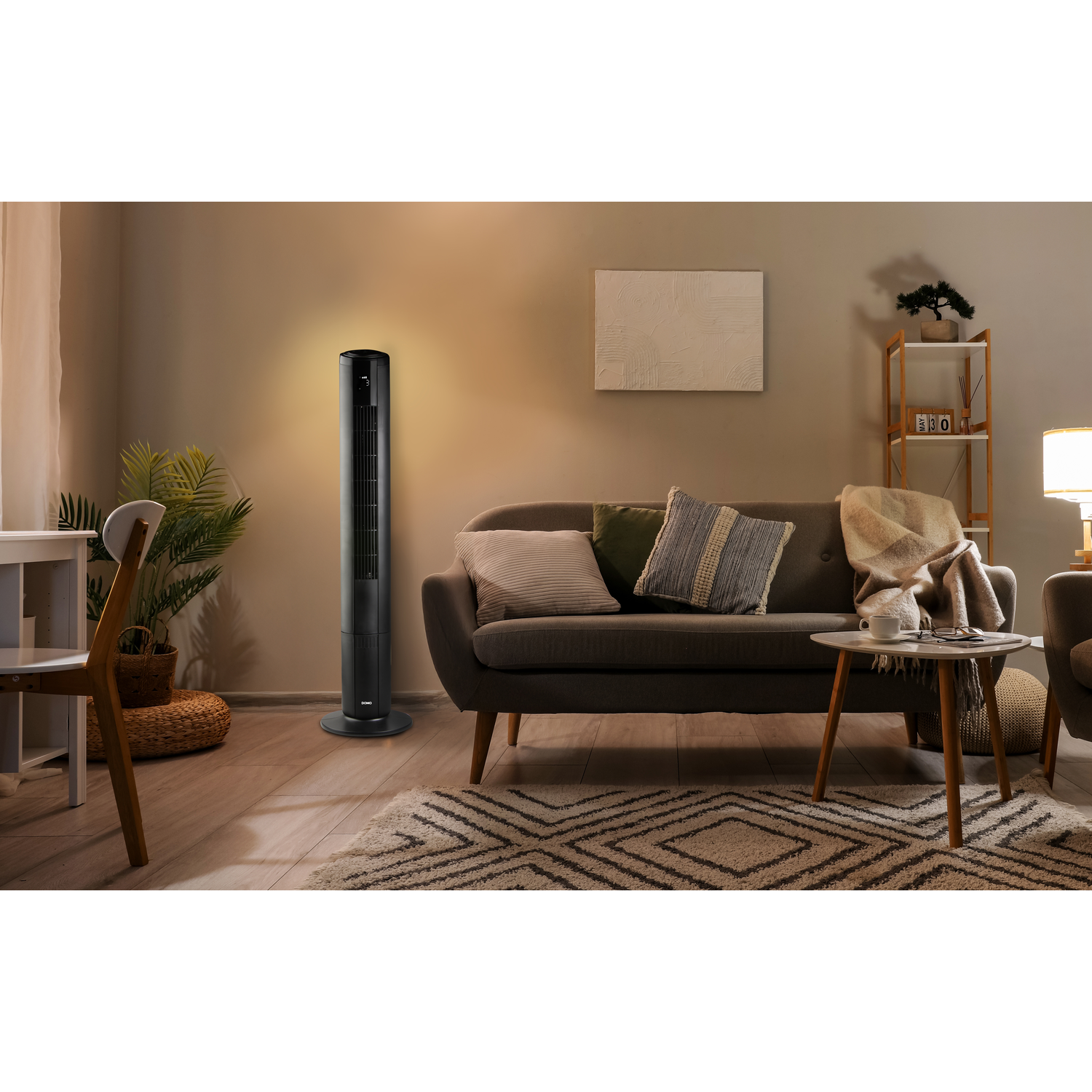 A slim black tower fan stands in a living room next to a sofa.