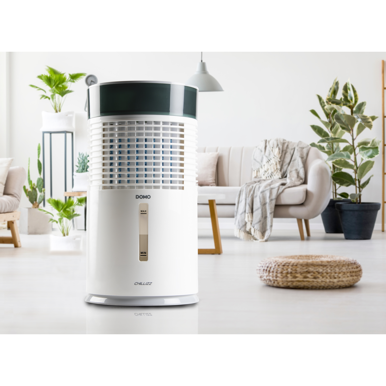 A white air cooler stands in a bright living room with a sofa and plants.