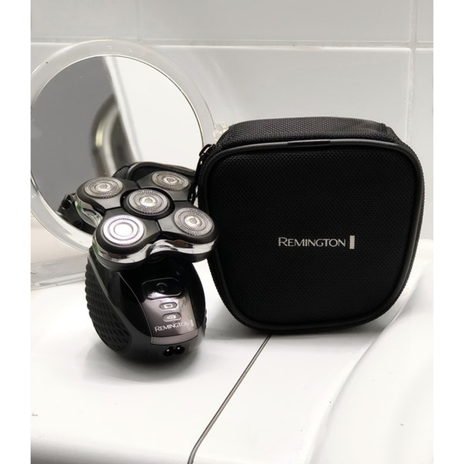 Rasoio Remington nero con testina a lamina e custodia accanto a specchio rotondo.