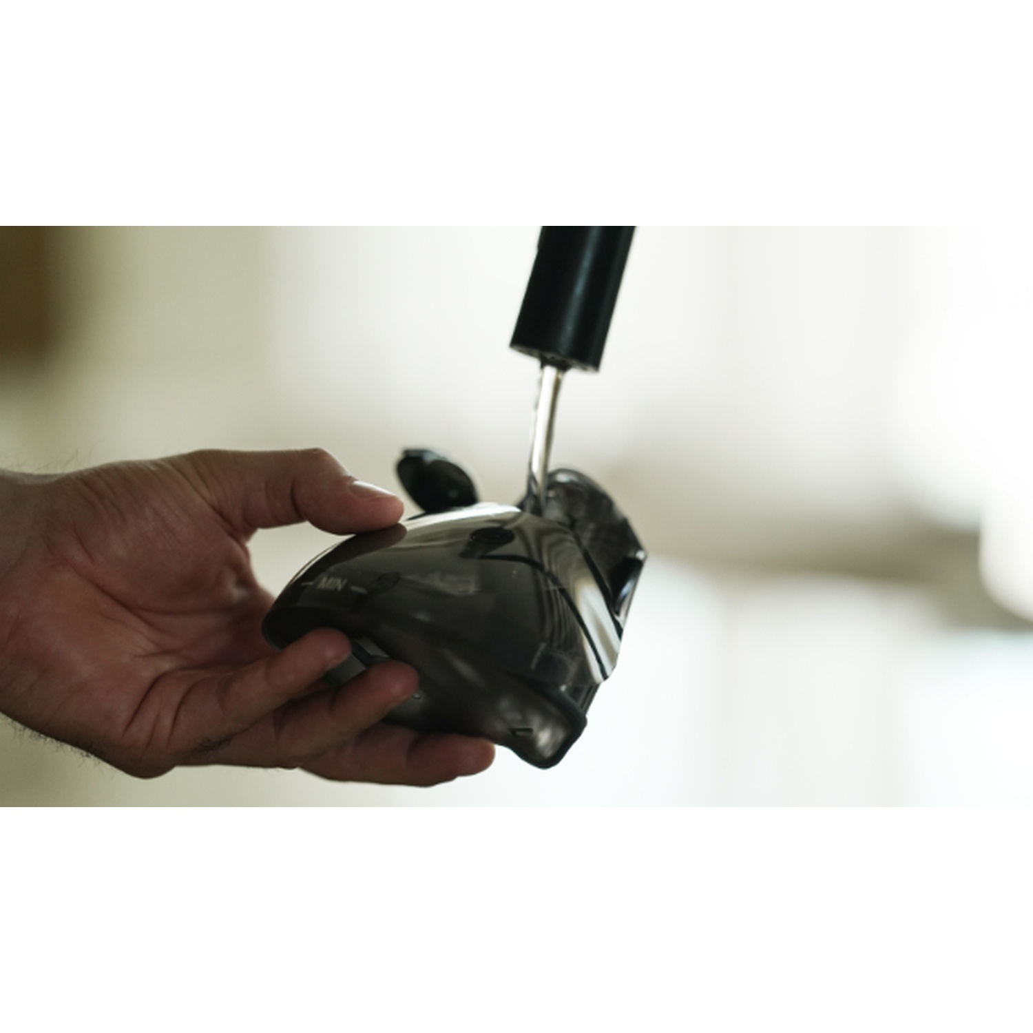 Une main tient un capuchon noir transparent pendant que l'eau y coule.
