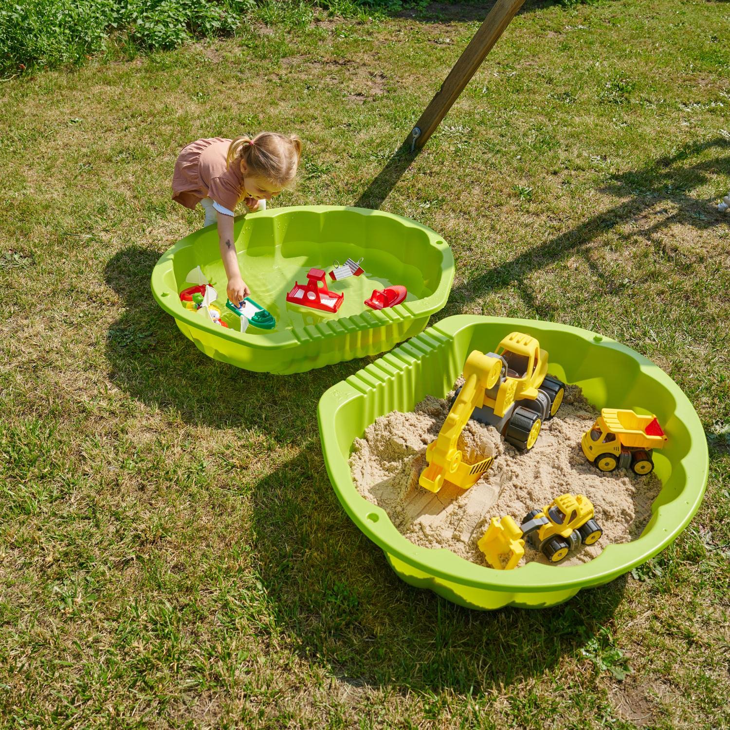 Ein kleines Mädchen spielt mit Wasserspielzeug in einer grünen Sandkastenwanne.