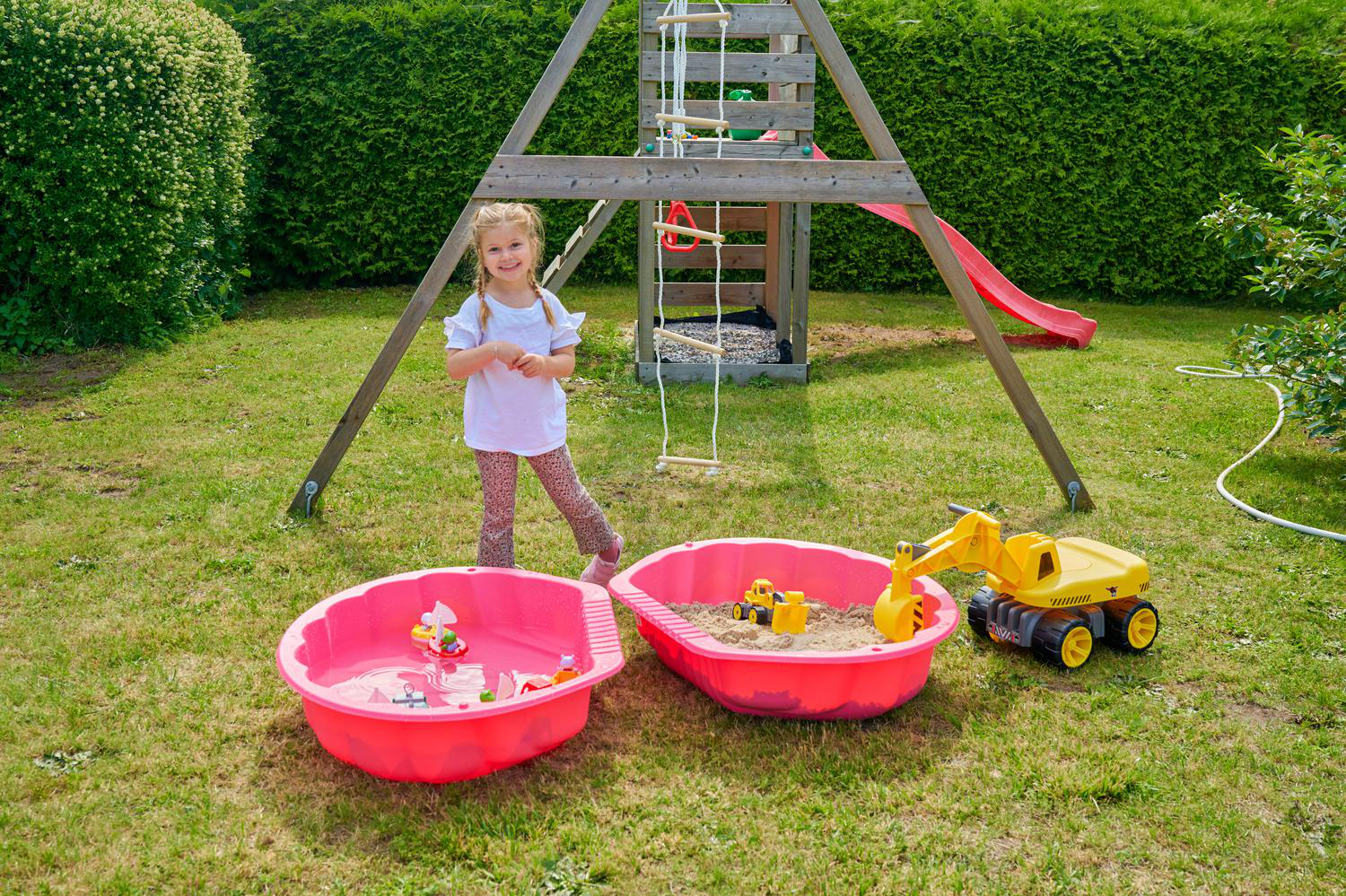 Ein Mädchen steht neben zwei Sandkästen und einem Spielgerüst im Garten.