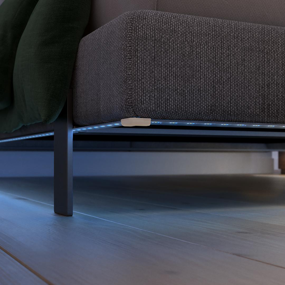 Graues Sofa mit blauen LED-Streifen unter dem Bett und dunklen Kissen.