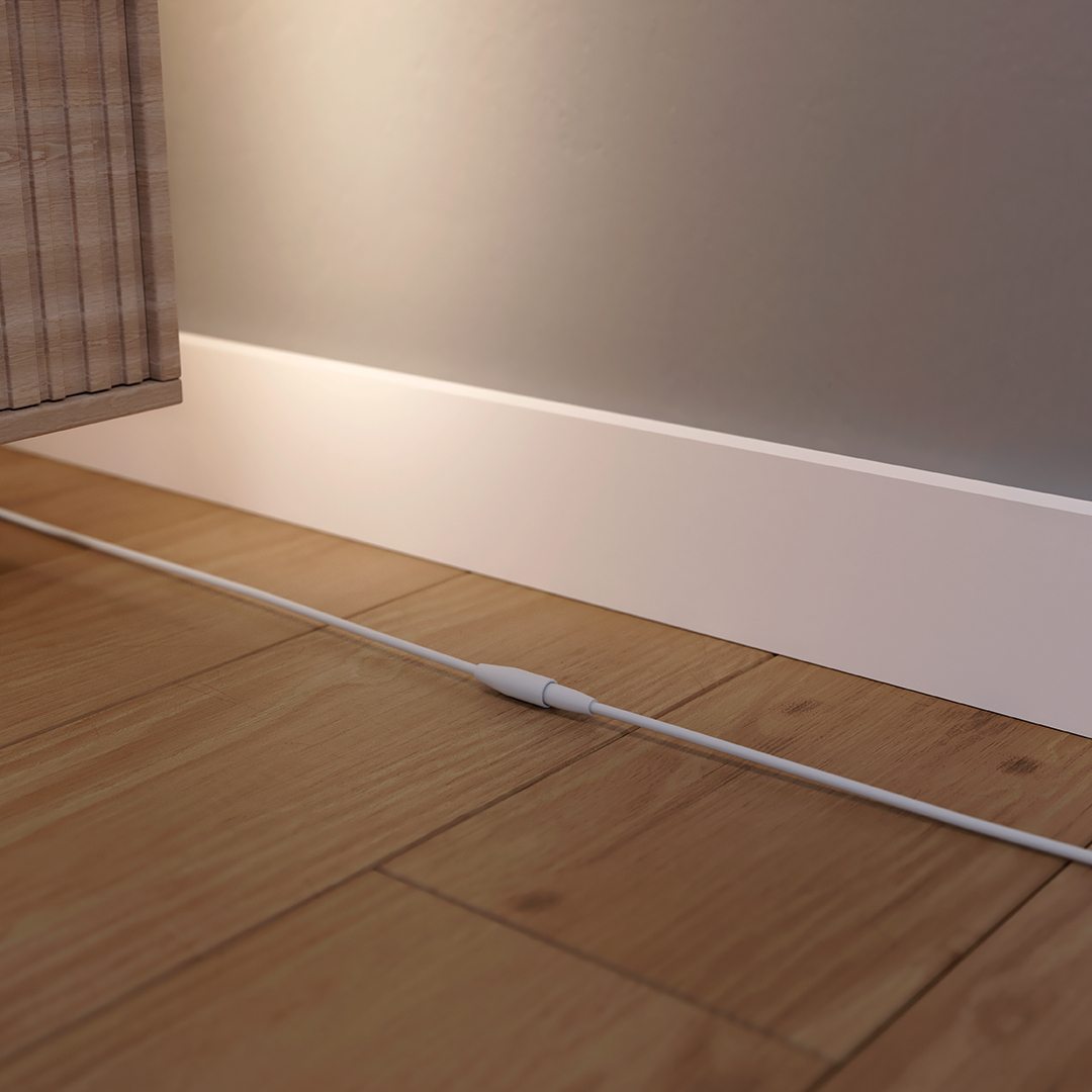 Ein weißes Kabel liegt auf einem Holzboden, neben einer Fußleiste und einem Möbelstück.