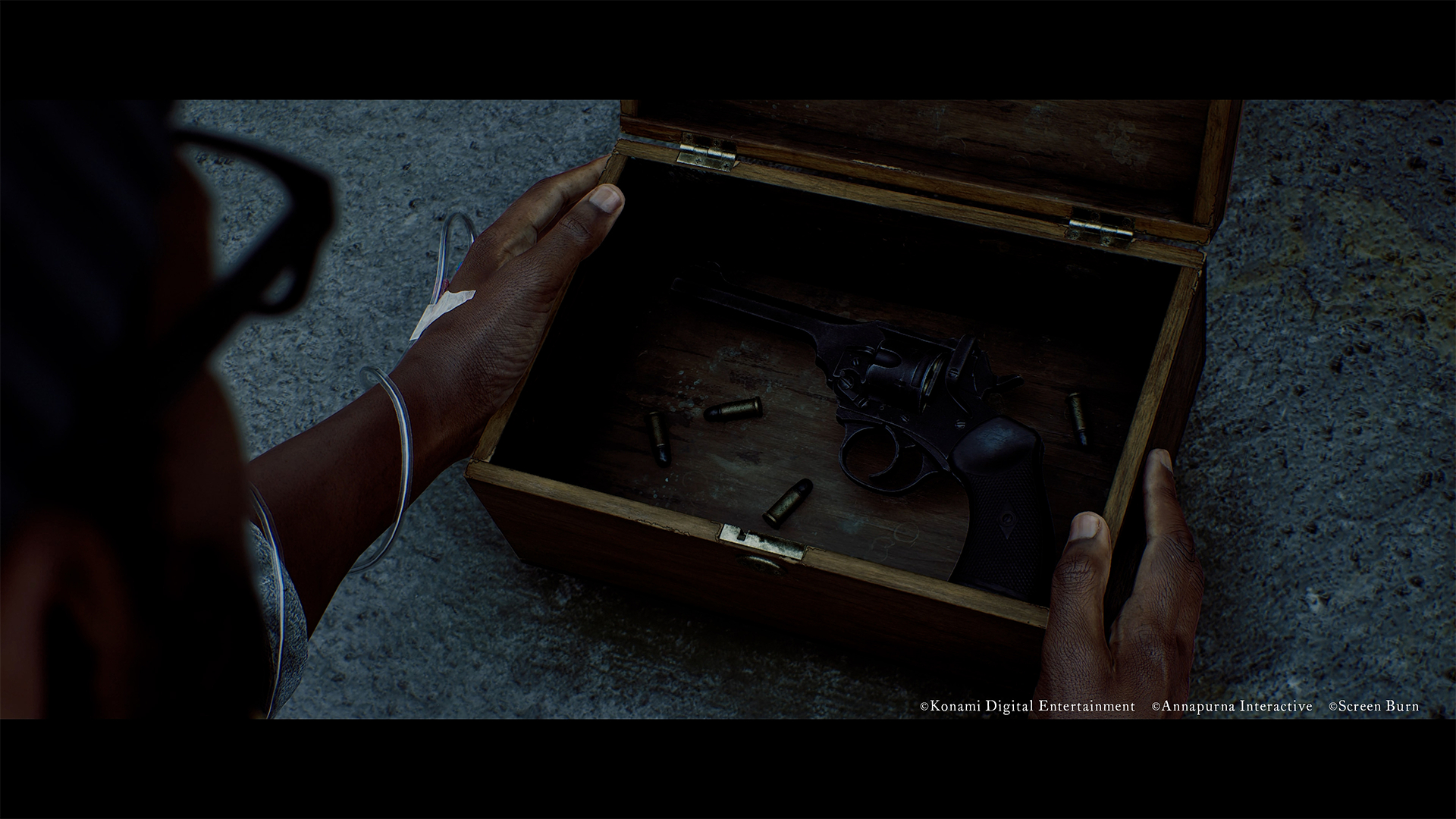 Dłoń otwiera drewniane pudełko z pistoletem i nabojami w środku.