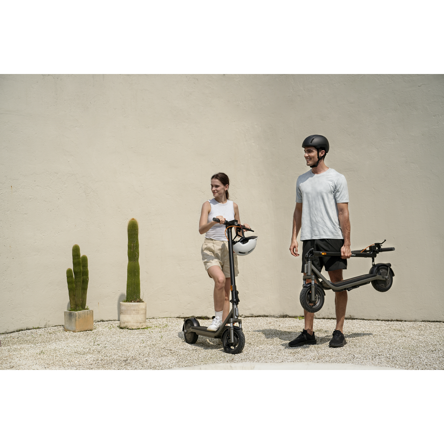 Man en vrouw met e-scooters voor een muur met cactussen.