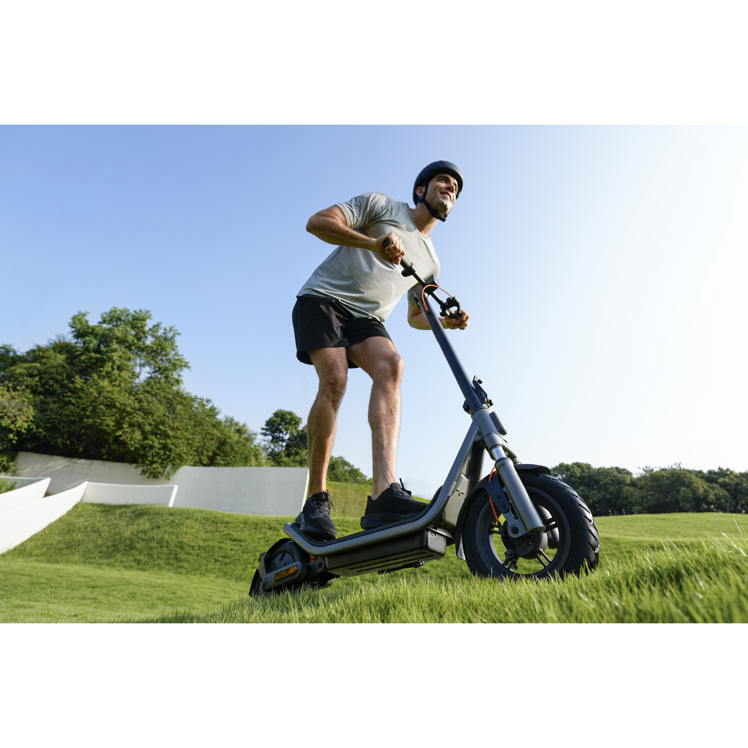 Man in helmet rides an electric scooter on a green lawn under a blue sky.