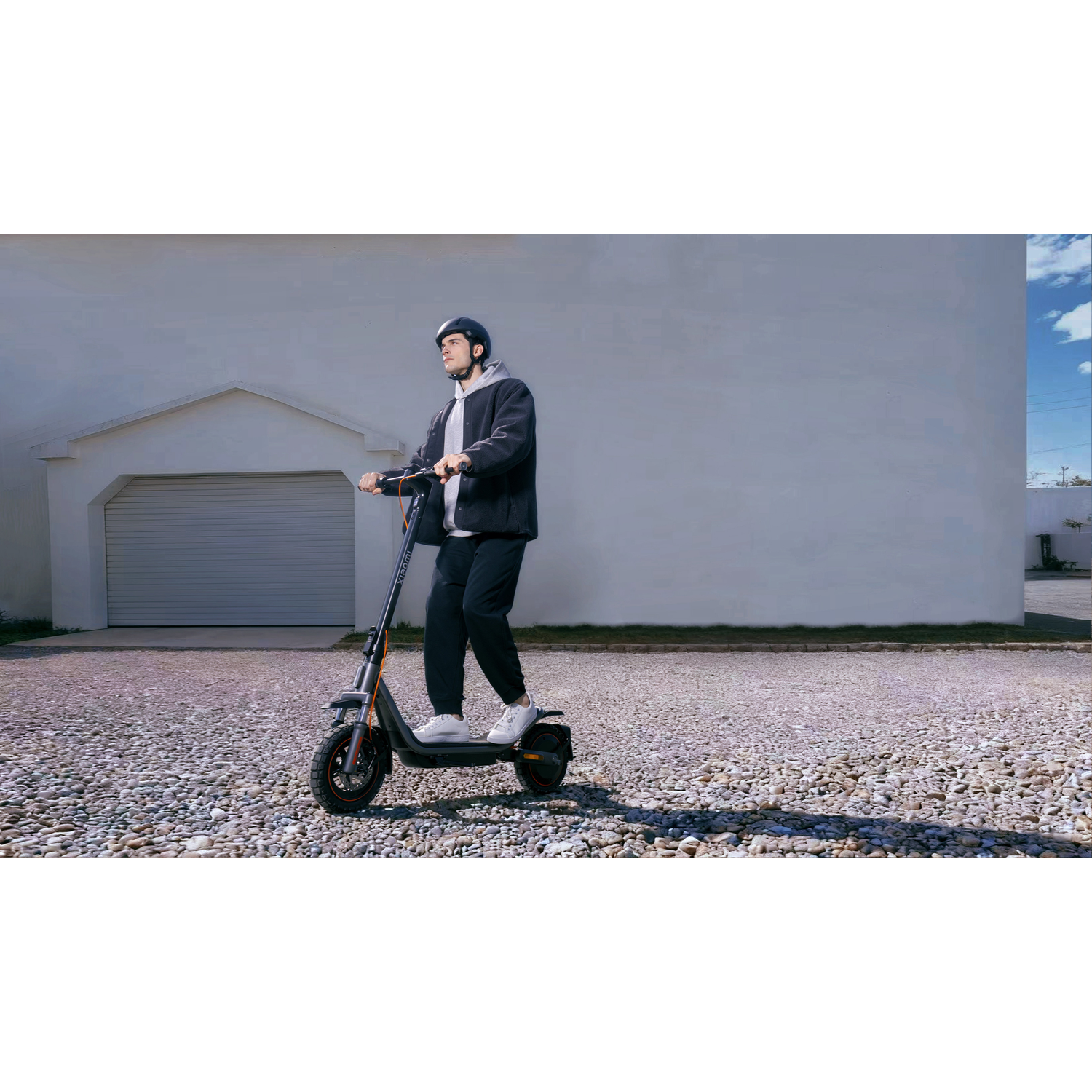 A man rides an electric scooter in front of a garage with a gray wall.