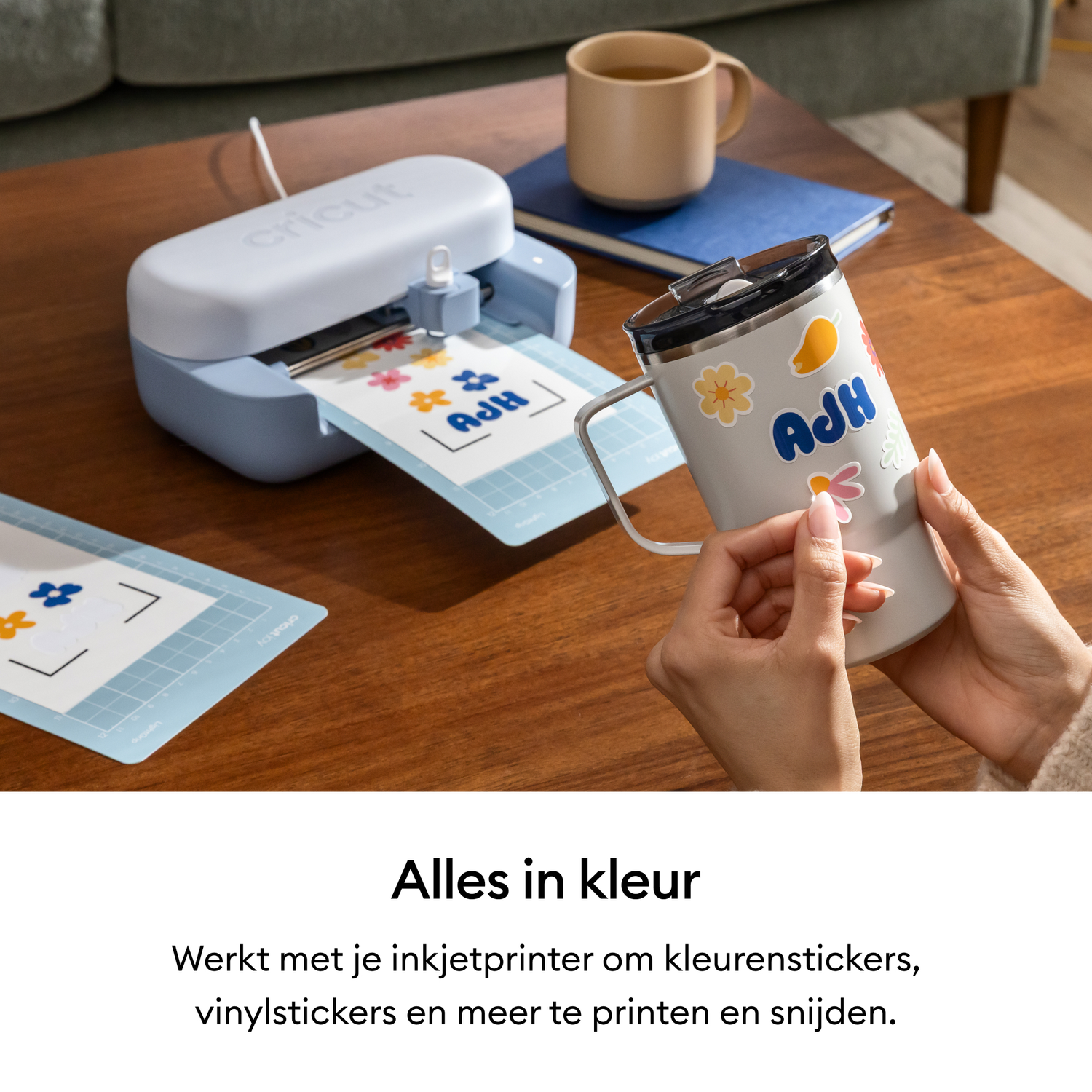 A cutting machine cuts colorful stickers, a hand applies them to a mug.
