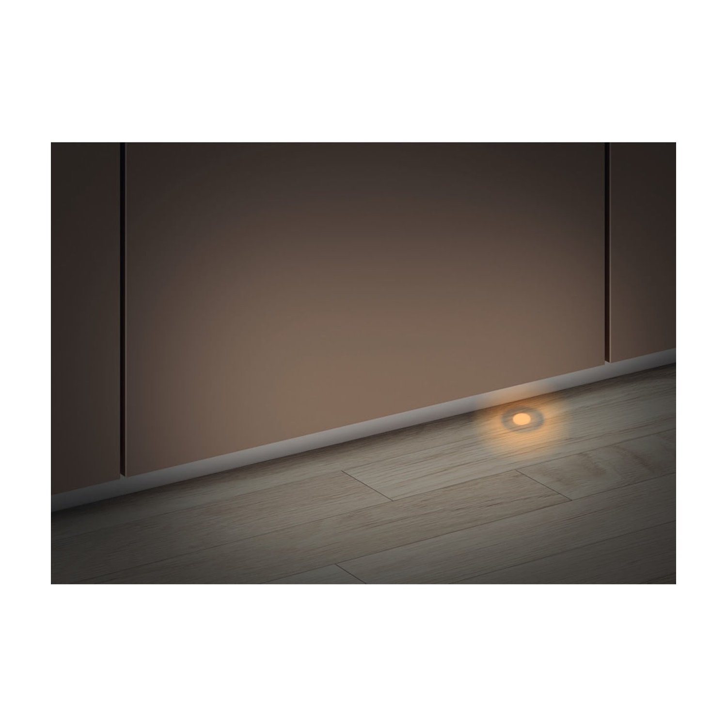 Una piccola luce rotonda da incasso emana un bagliore caldo su parquet.