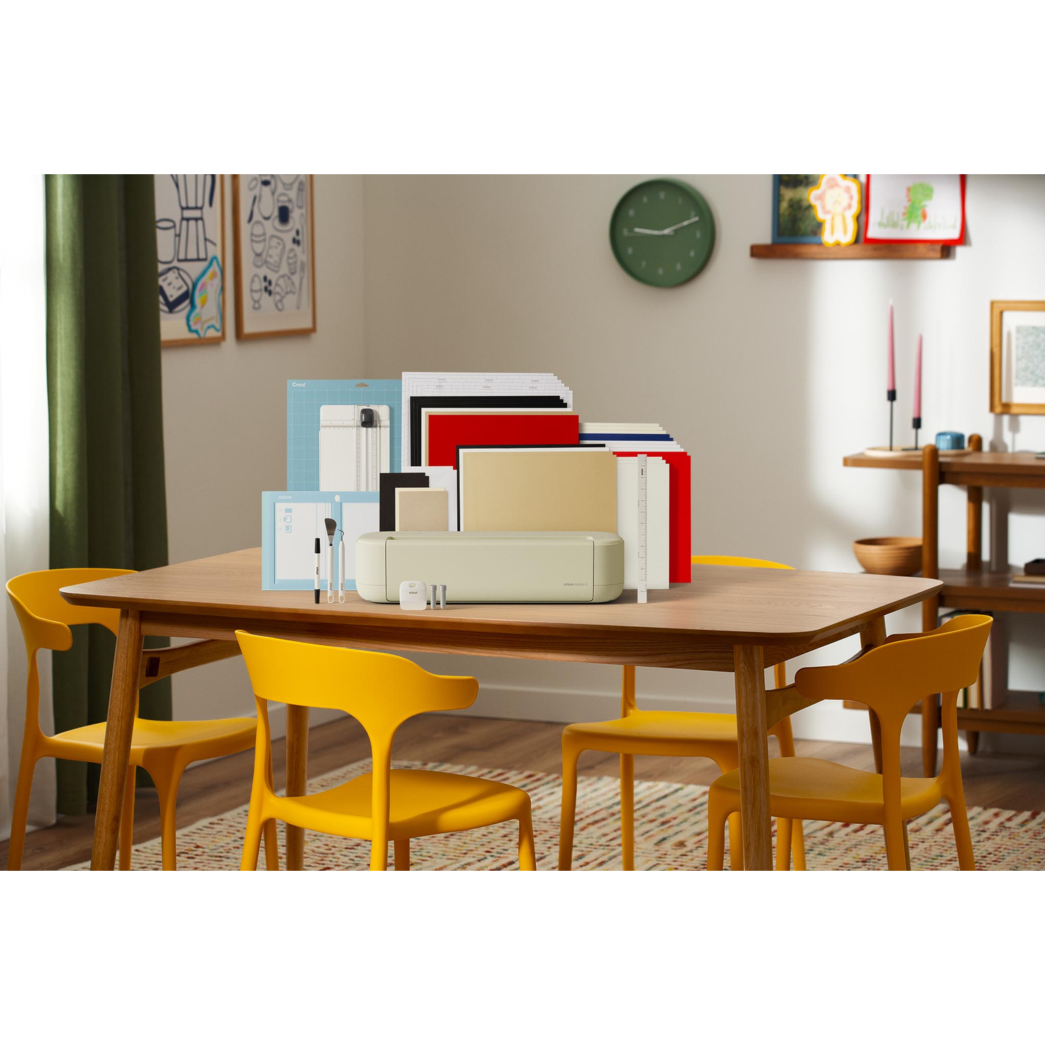 A cutting machine, paper stacks, and pens on a wooden table with yellow chairs.