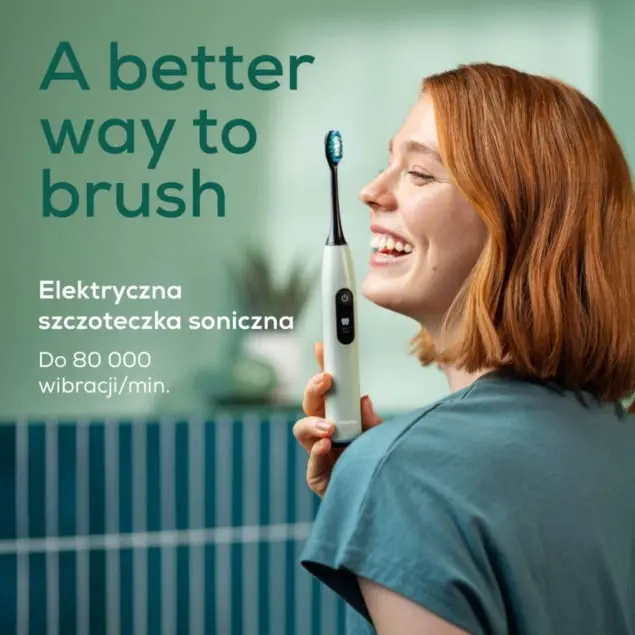 Uśmiechnięta kobieta trzyma białą, elektryczną szczoteczkę do zębów z niebieskim włosiem.