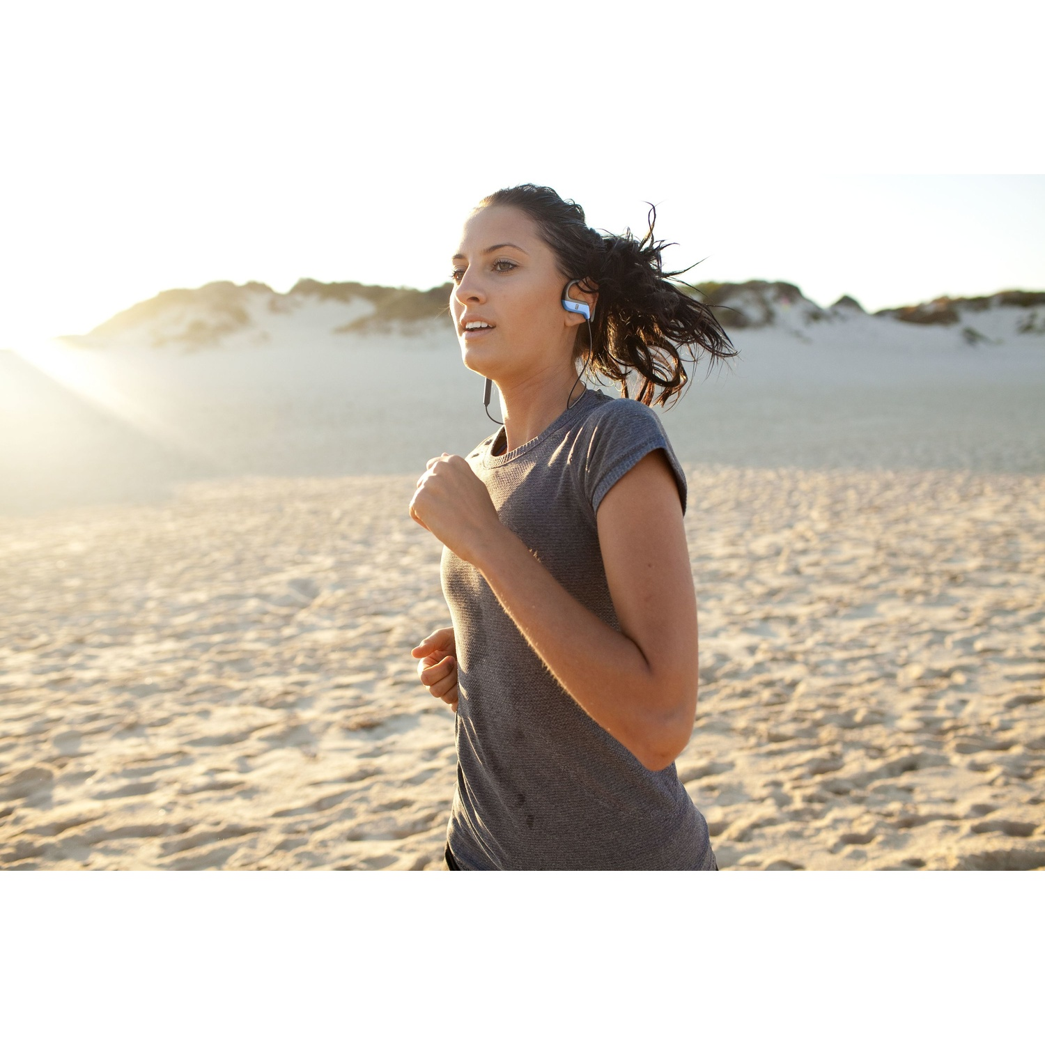 Una donna corre sulla spiaggia, al sole, con le cuffie.