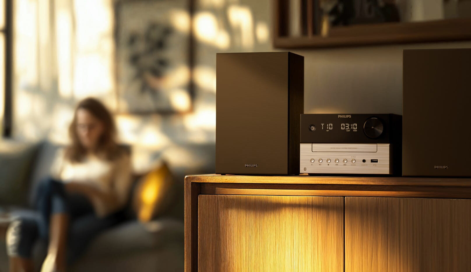 Kobieta siedzi na kanapie, system audio Philips stoi na drewnianej szafce.