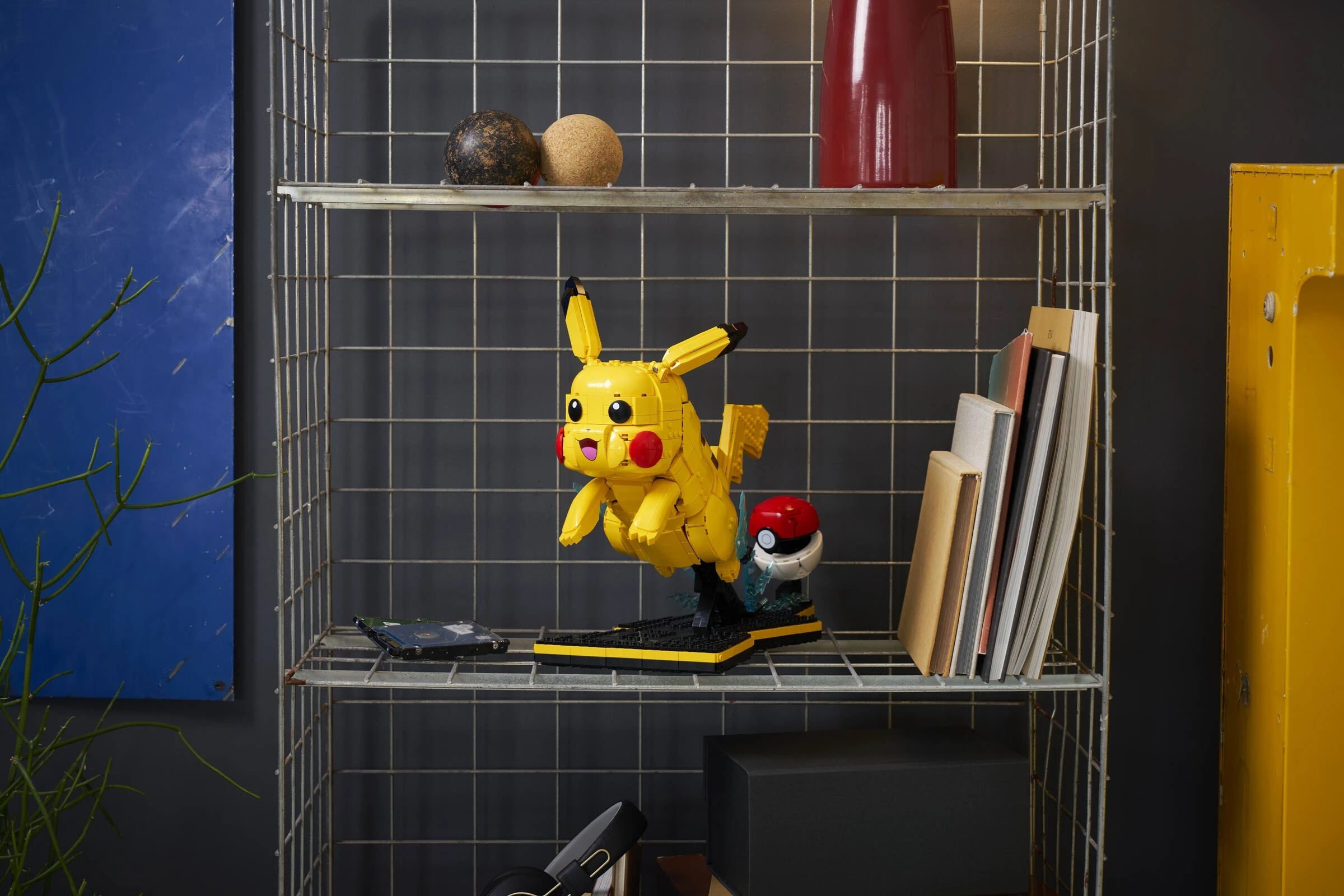 Żółty Lego Pikachu z Pokéballem stoi na półce. Obok są książki i dekoracje.