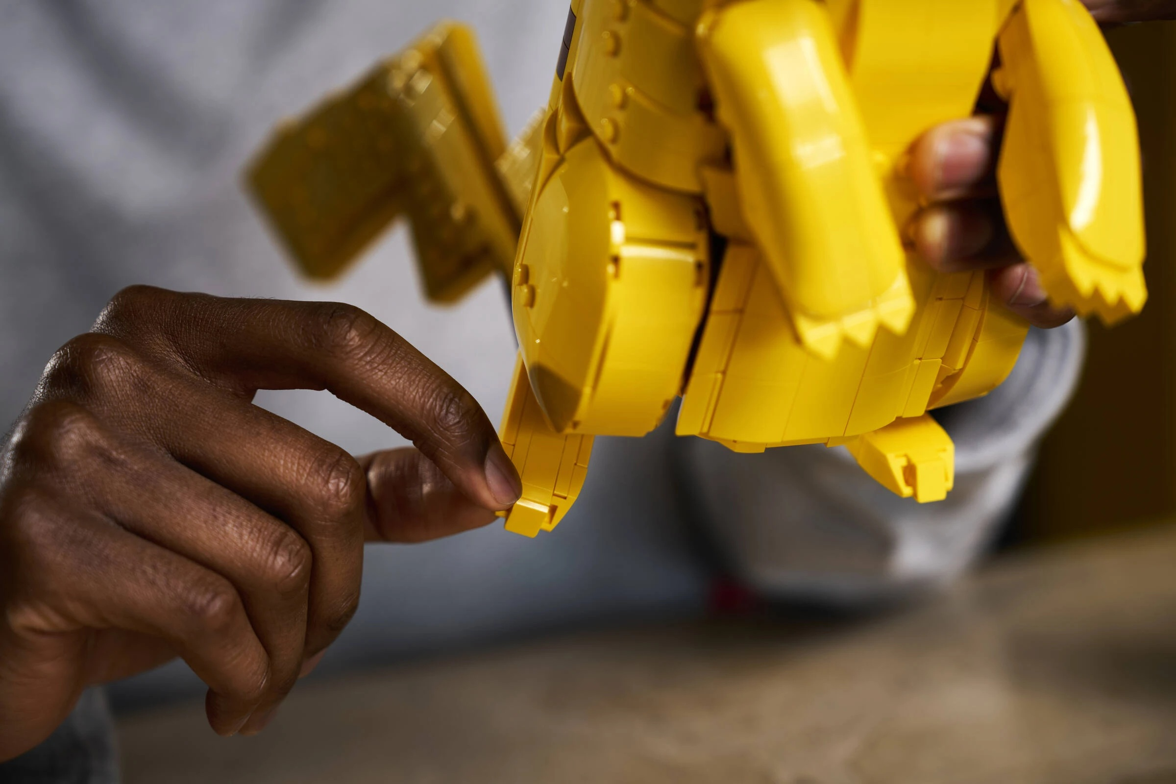 Ręka buduje żółtego Pikachu z klocków Lego.