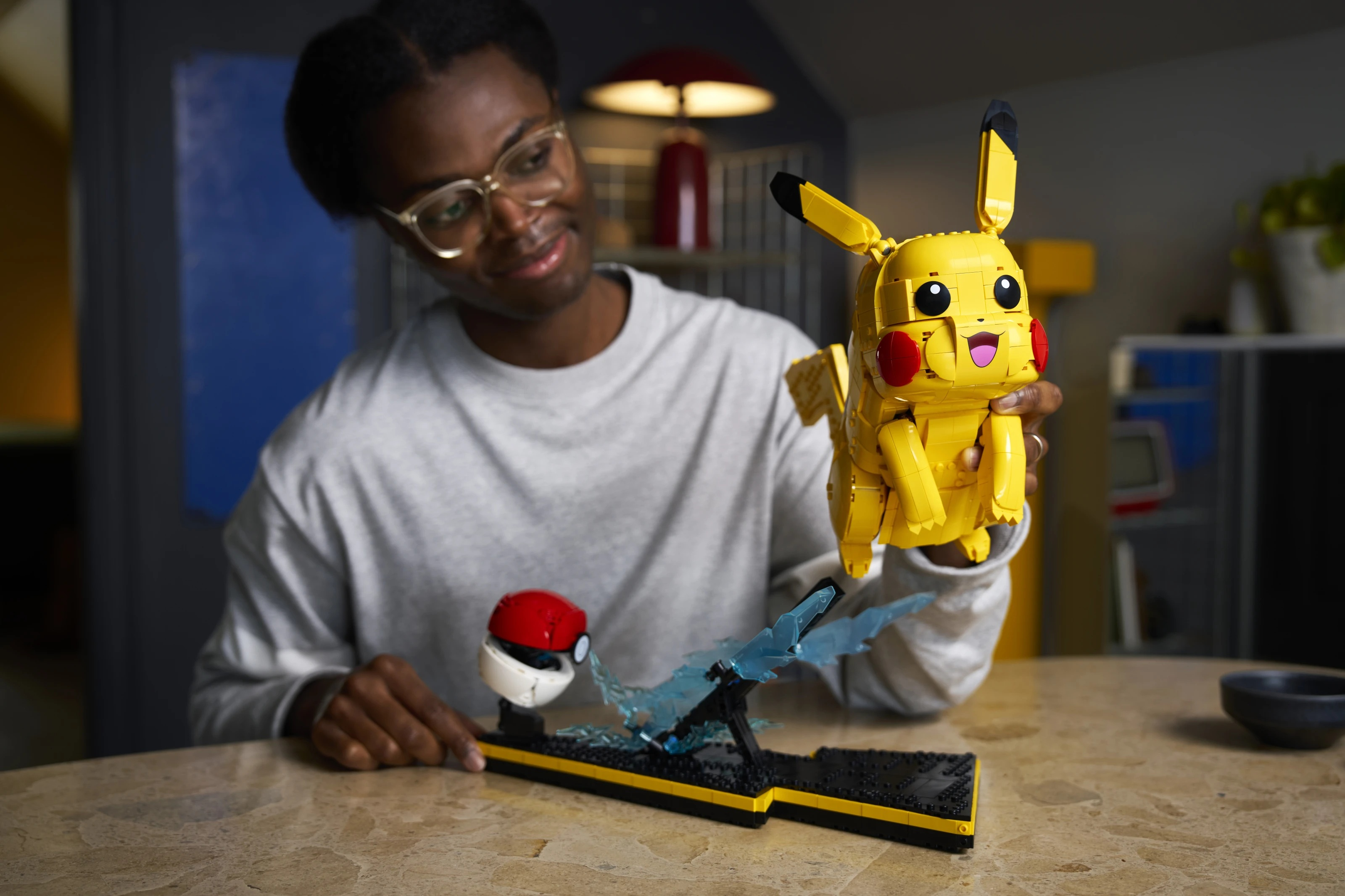 Osoba trzymająca żółty model Pikachu z LEGO obok Pokeballa i niebieskich elementów błyskawic.