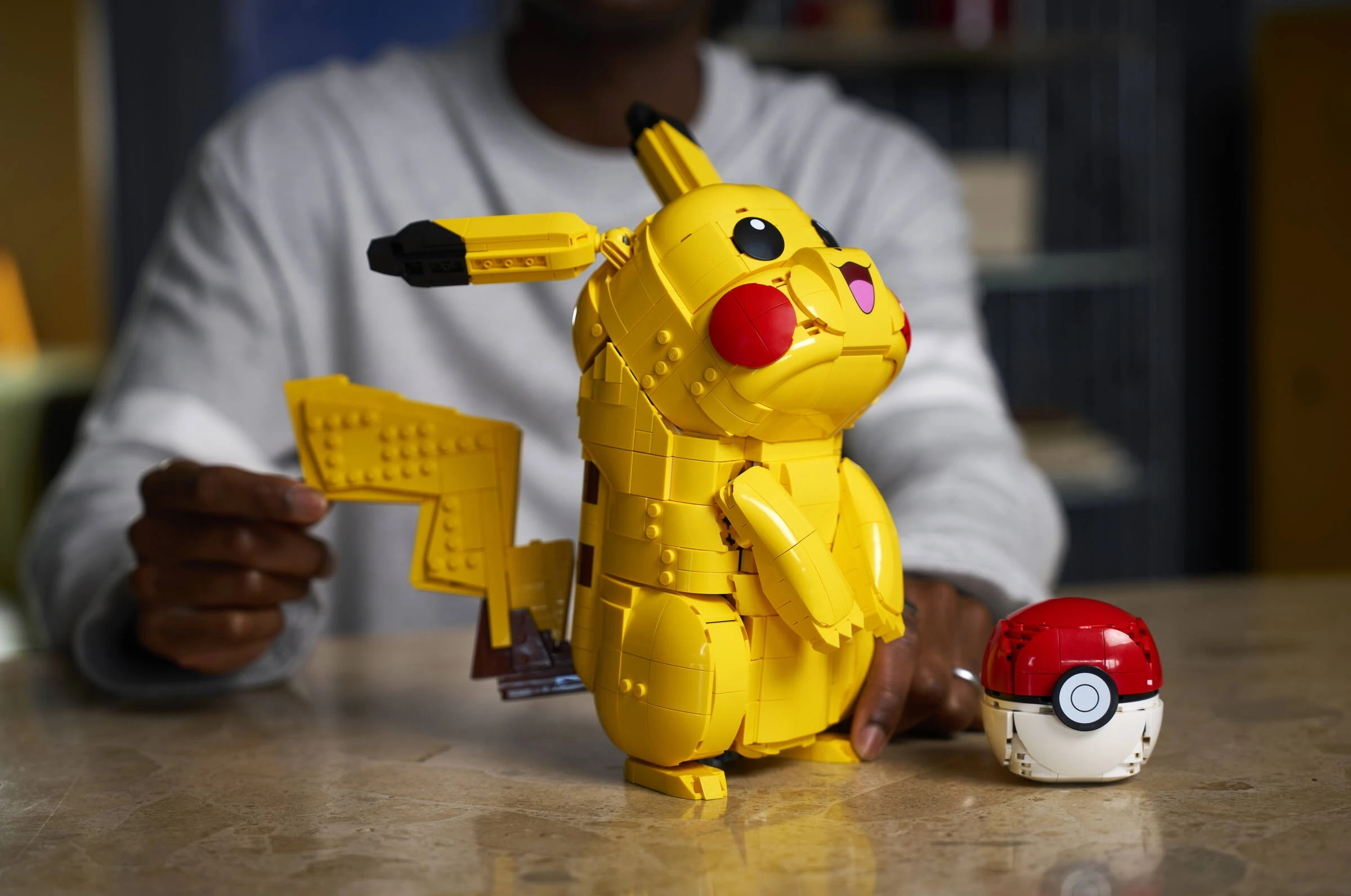 Mężczyzna buduje żółtego Pikachu z Lego i Pokeballa na stole.