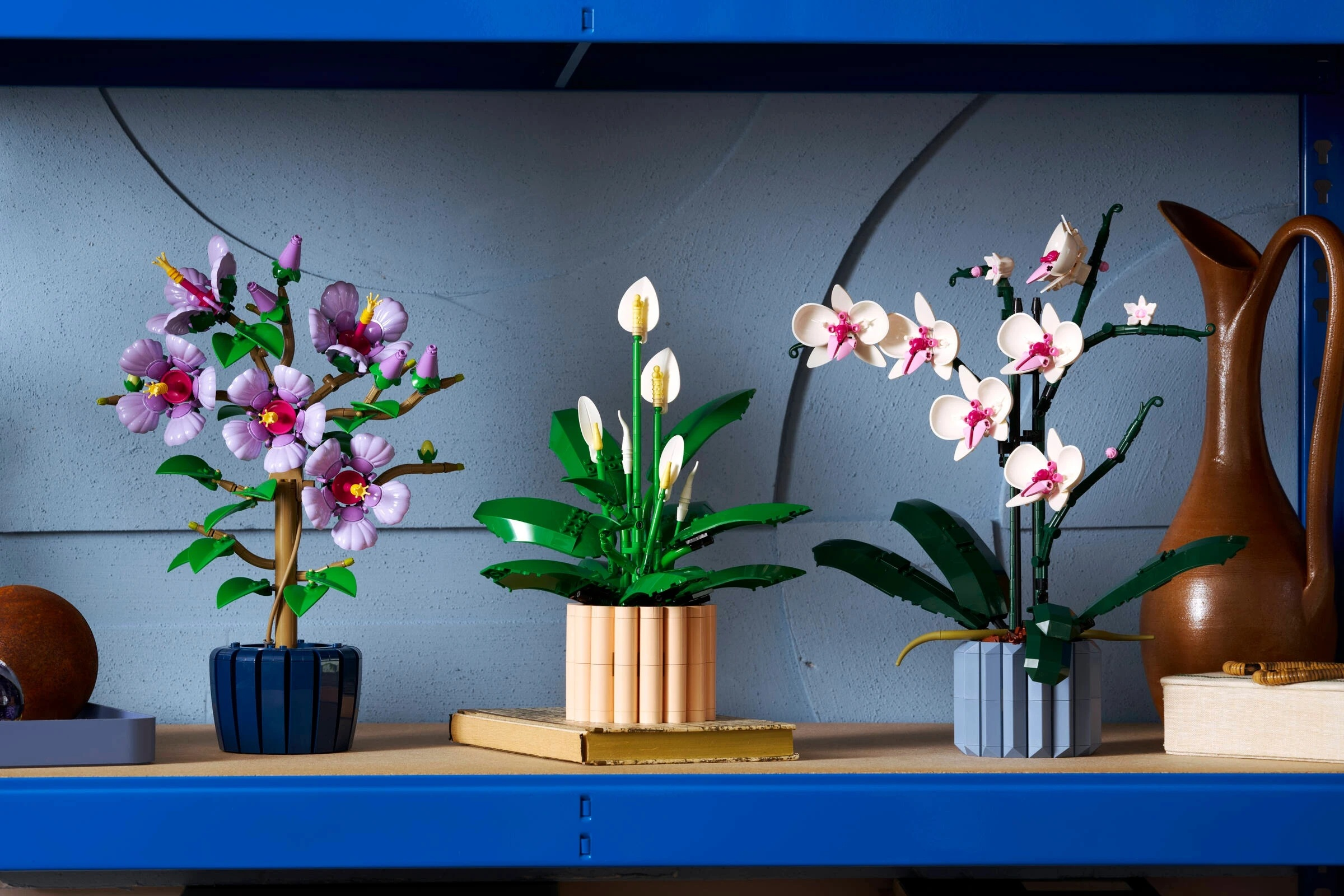 Trzy kompozycje kwiatowe LEGO: fioletowy hibiskus, białe orchidee i anturium.